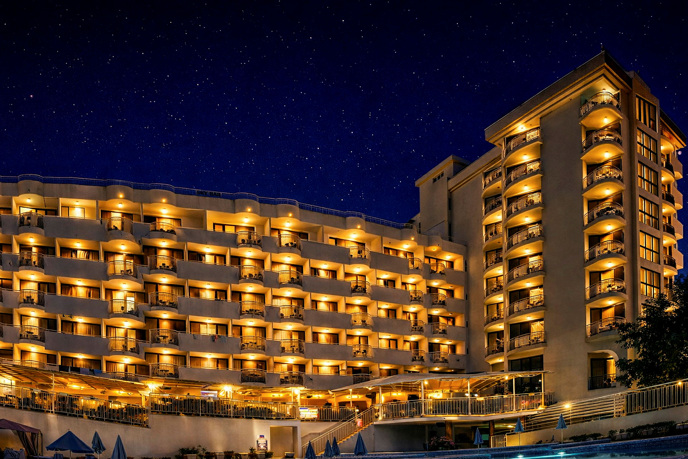 Hotellbyggnad med belysta balkonger och fönster vid kvällstid under en stjärnklar natthimmel. (AI-genererad text)