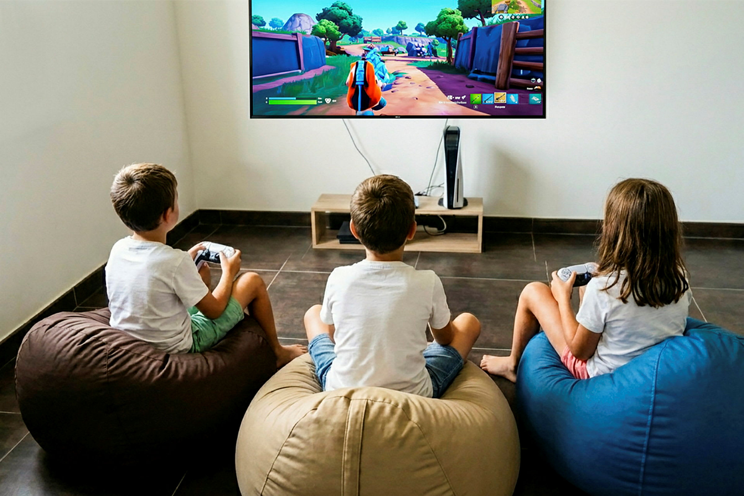 Tre barn sitter på sittsäckar och spelar ett videospel på en stor TV som är monterad på väggen. (AI-genererad text)