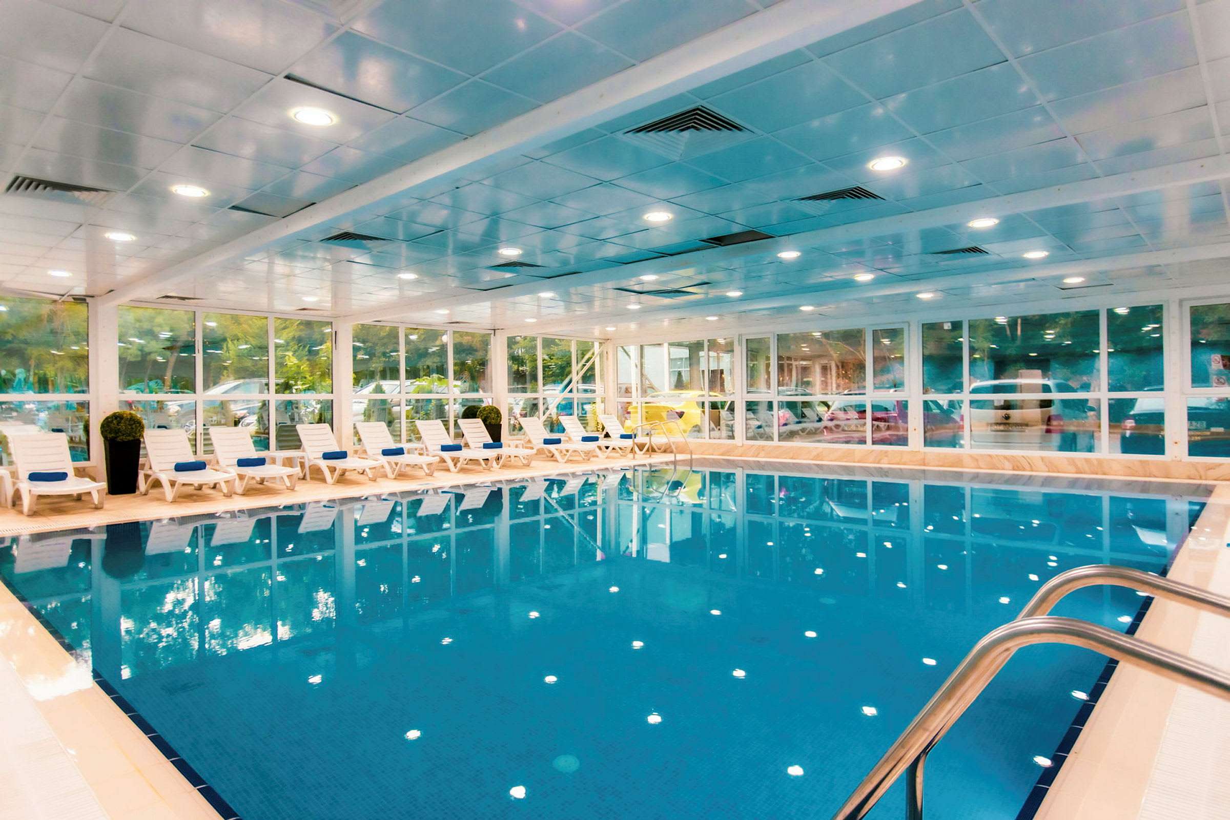 Inomhuspool med klarblått vatten och solstolar längs ena sidan. (AI-genererad text)