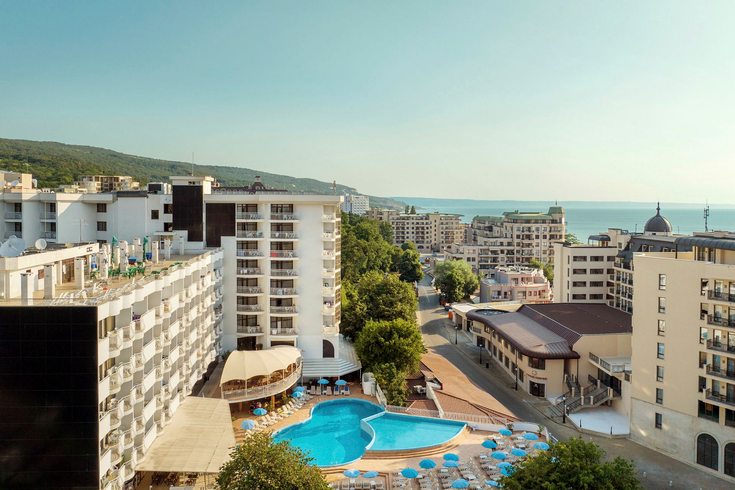 Hotellbyggnader med en pool i förgrunden och havet i bakgrunden. (AI-genererad text)