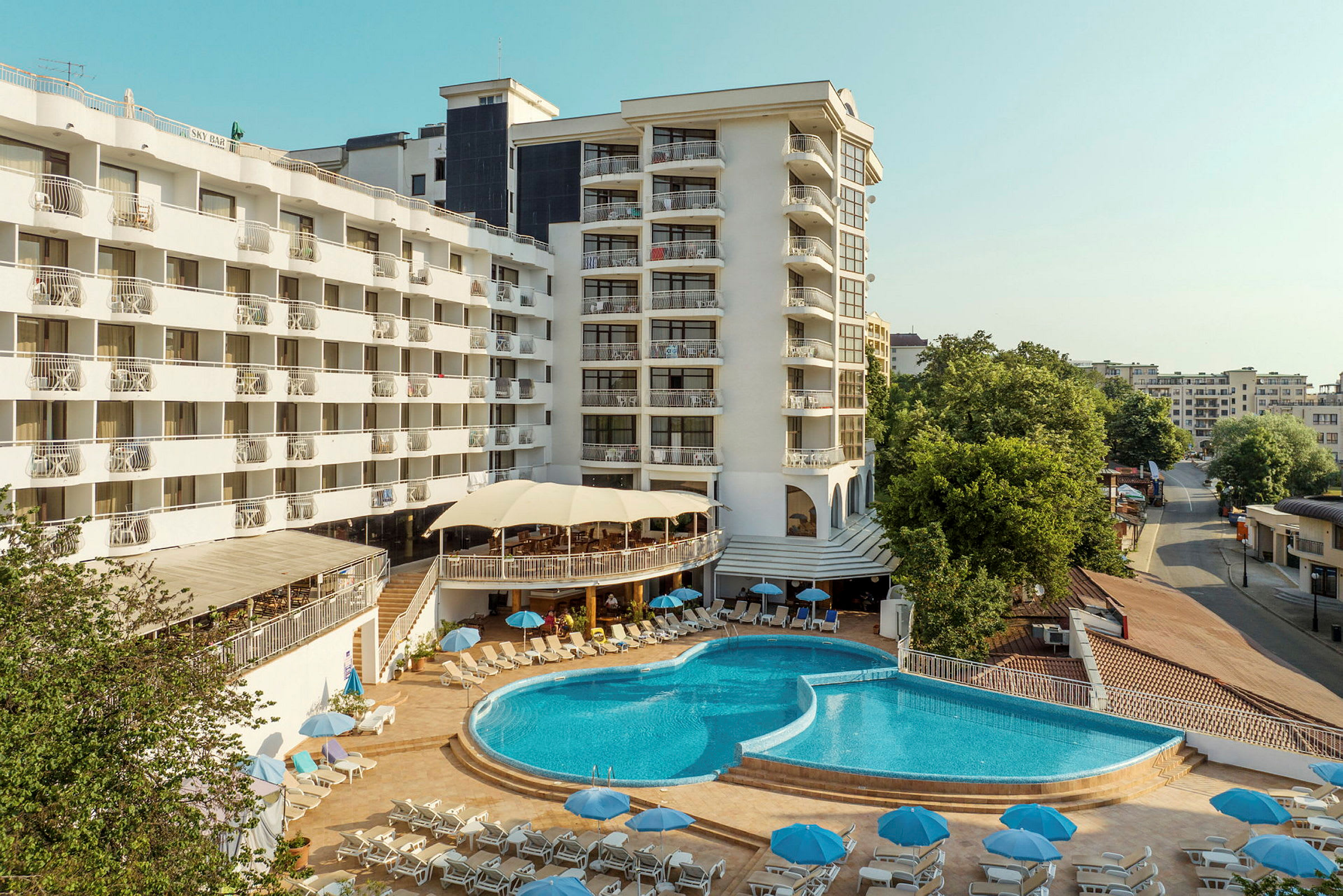 Hotellkomplex med en stor pool och solstolar omgivna av byggnader. (AI-genererad text)