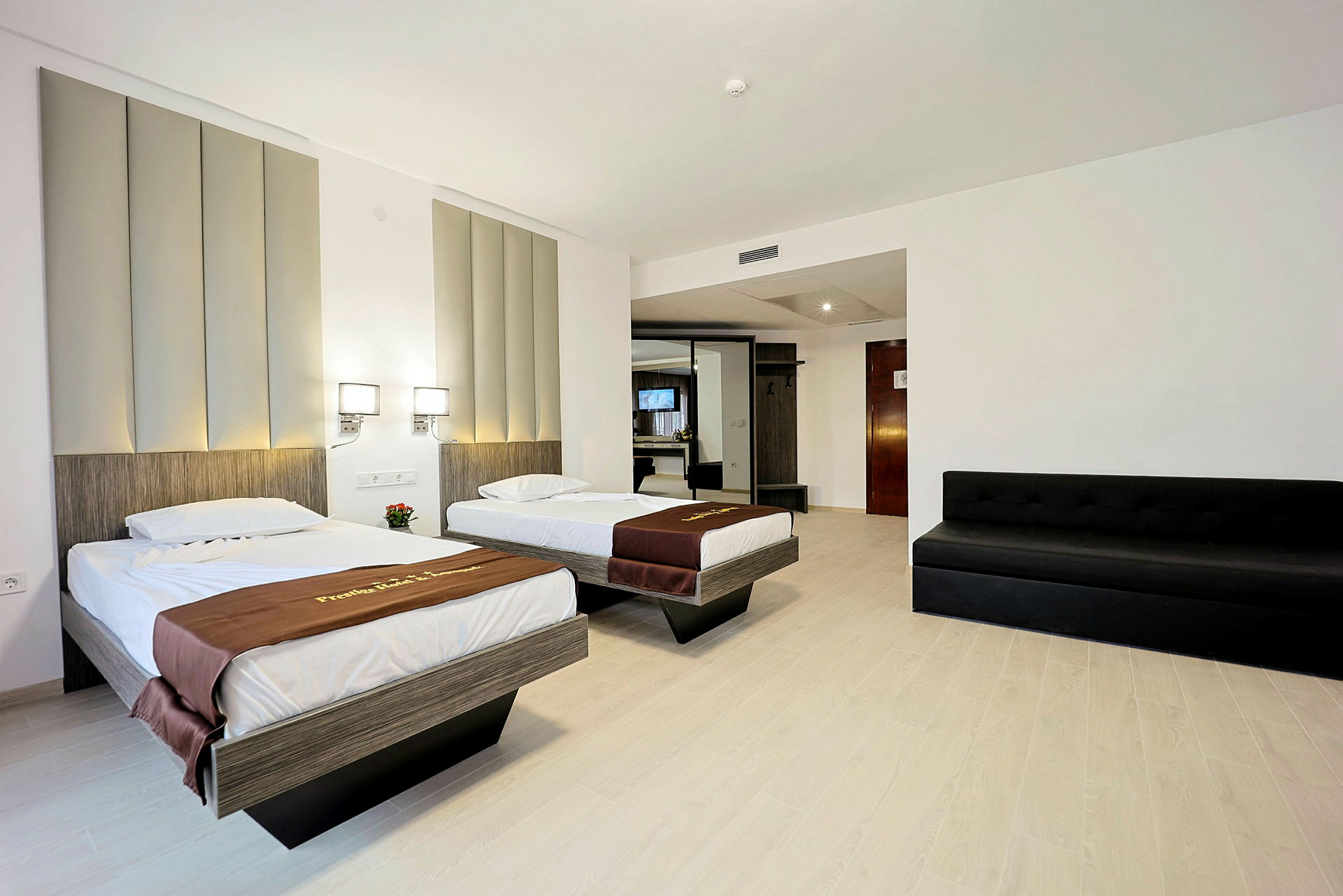 Hotellrum med två enkelsängar, en svart soffa och modernt inrett med en garderob samt spegel. (AI-genererad text)