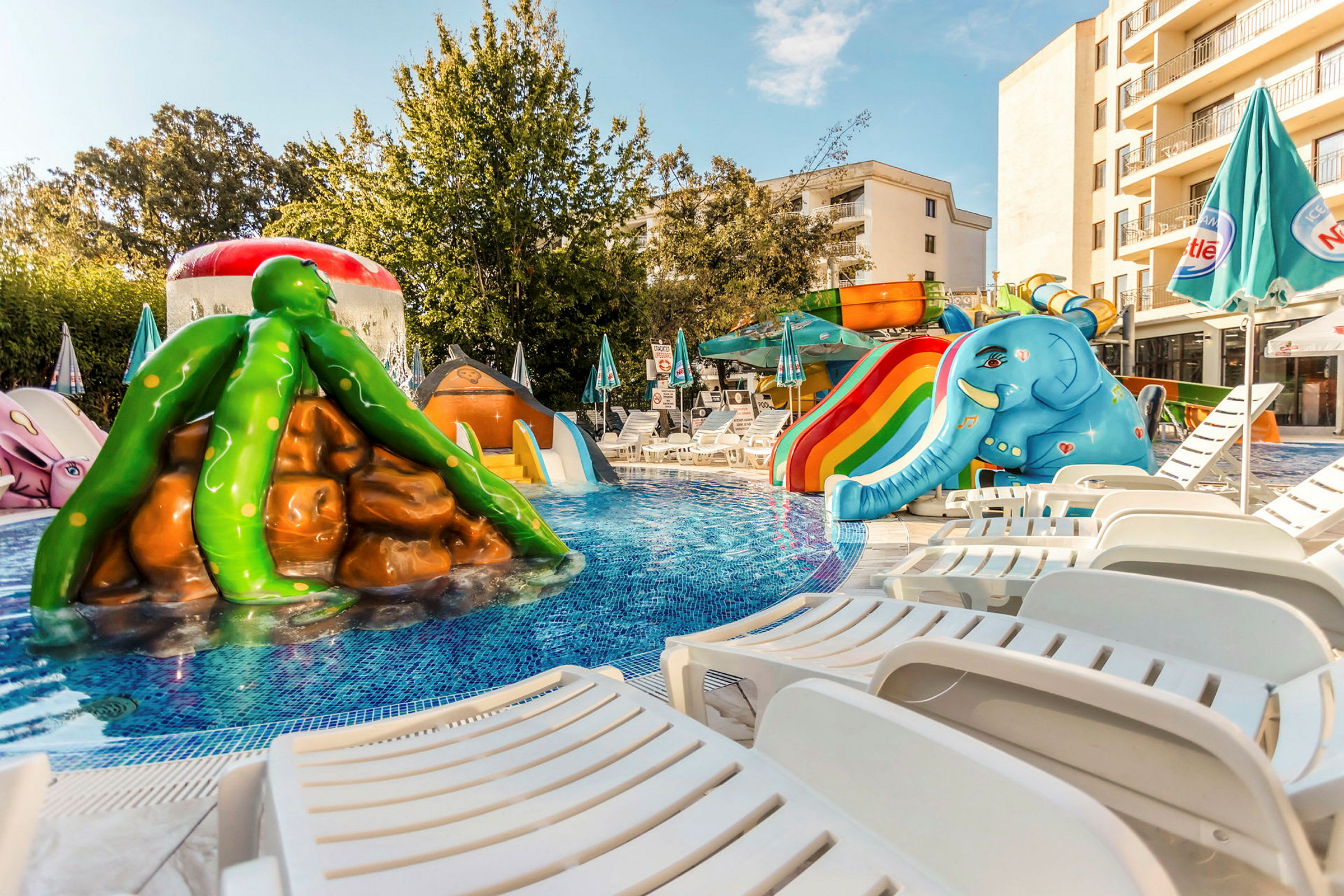 En pool med vattenrutschkanor och figurer i färgglada motiv, omgiven av solstolar. (AI-genererad text)