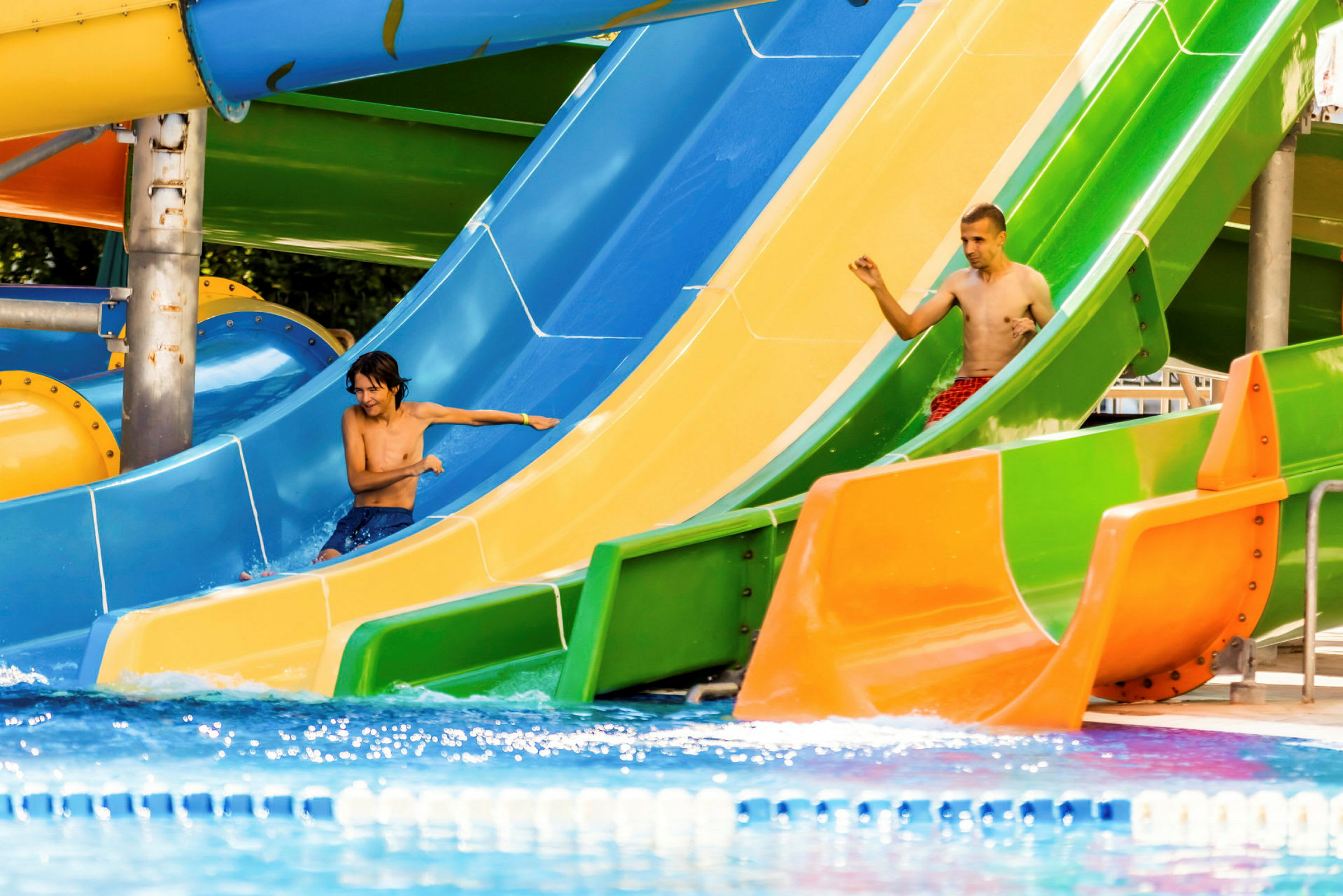 Två personer åker nerför färgglada vattenrutschbanor vid en pool. (AI-genererad text)