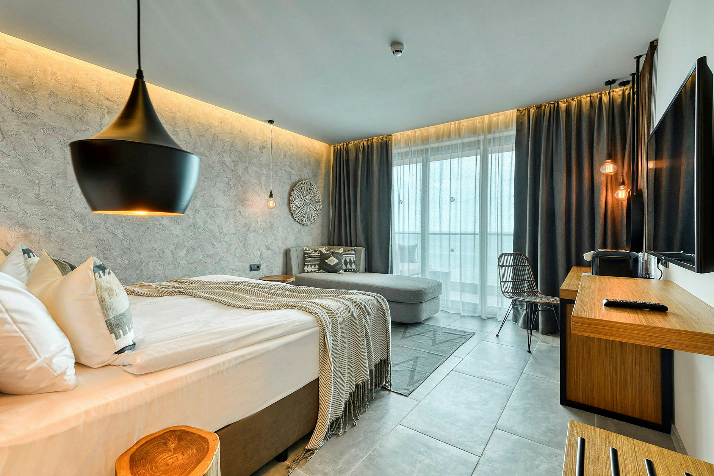 Ett modernt hotellrum med säng, soffa, skrivbord och stora fönster. (AI-genererad text)
