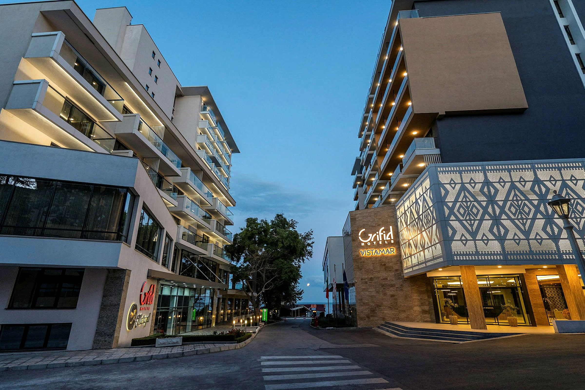 Två moderna hotellbyggnader vid en gångväg på kvällen. (AI-genererad text)