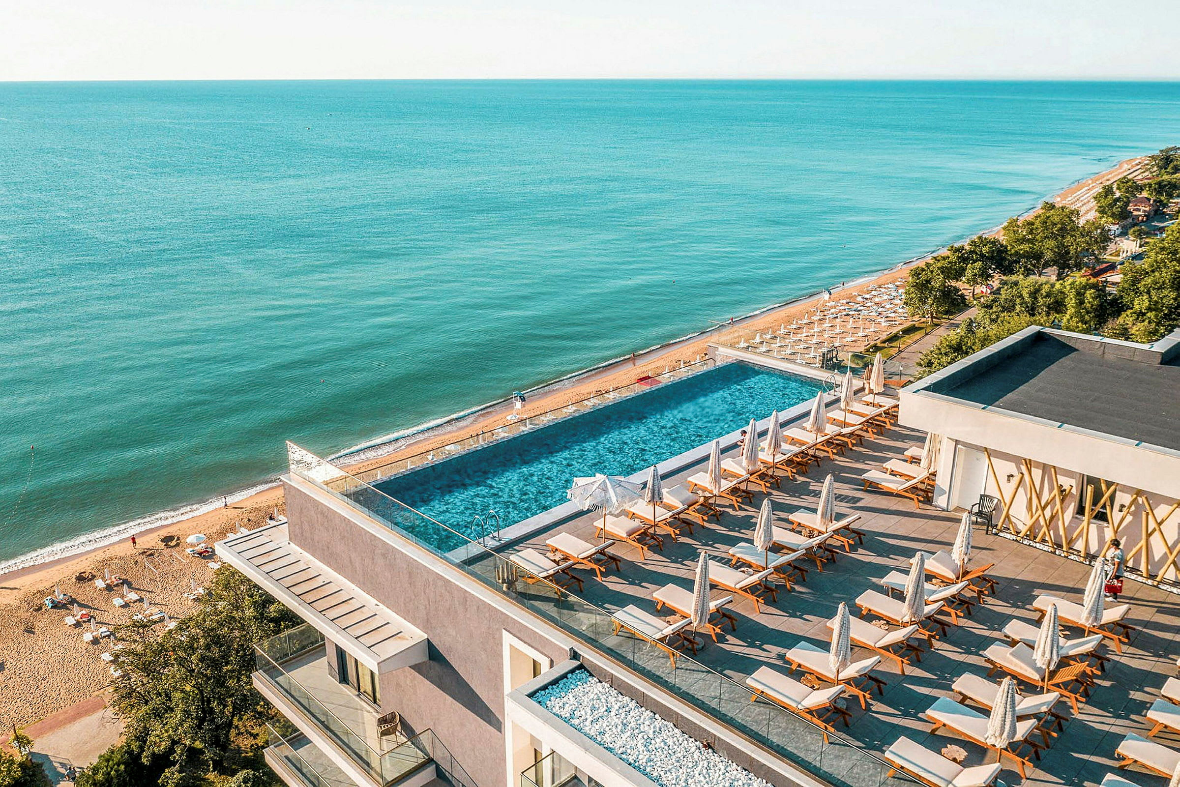 En pool med solstolar på en terrass med utsikt över stranden och havet. (AI-genererad text)