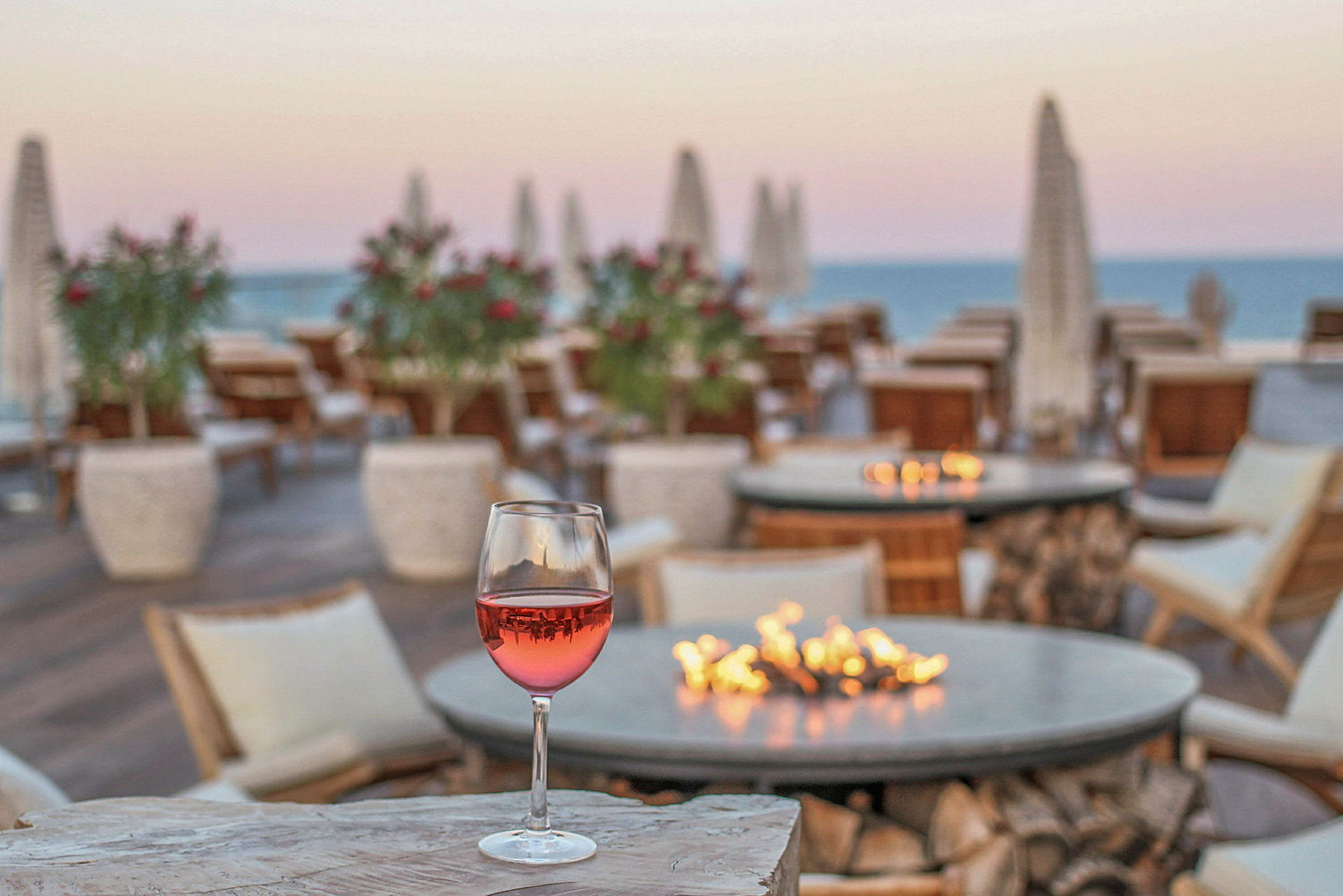 Ett glas rosévin står på en stenbord i en utomhusrestaurang med utsikt mot havet och solnedgången. (AI-genererad text)