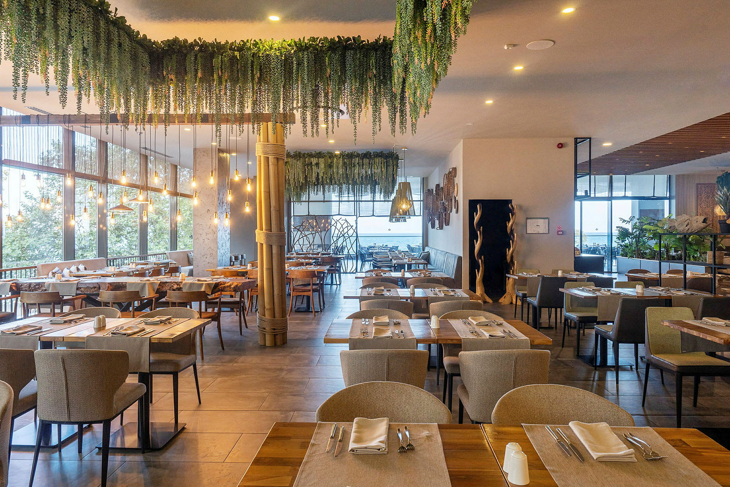 En restaurang med bord dukade för servering, omgiven av grön dekoration och ljuskällor. (AI-genererad text)