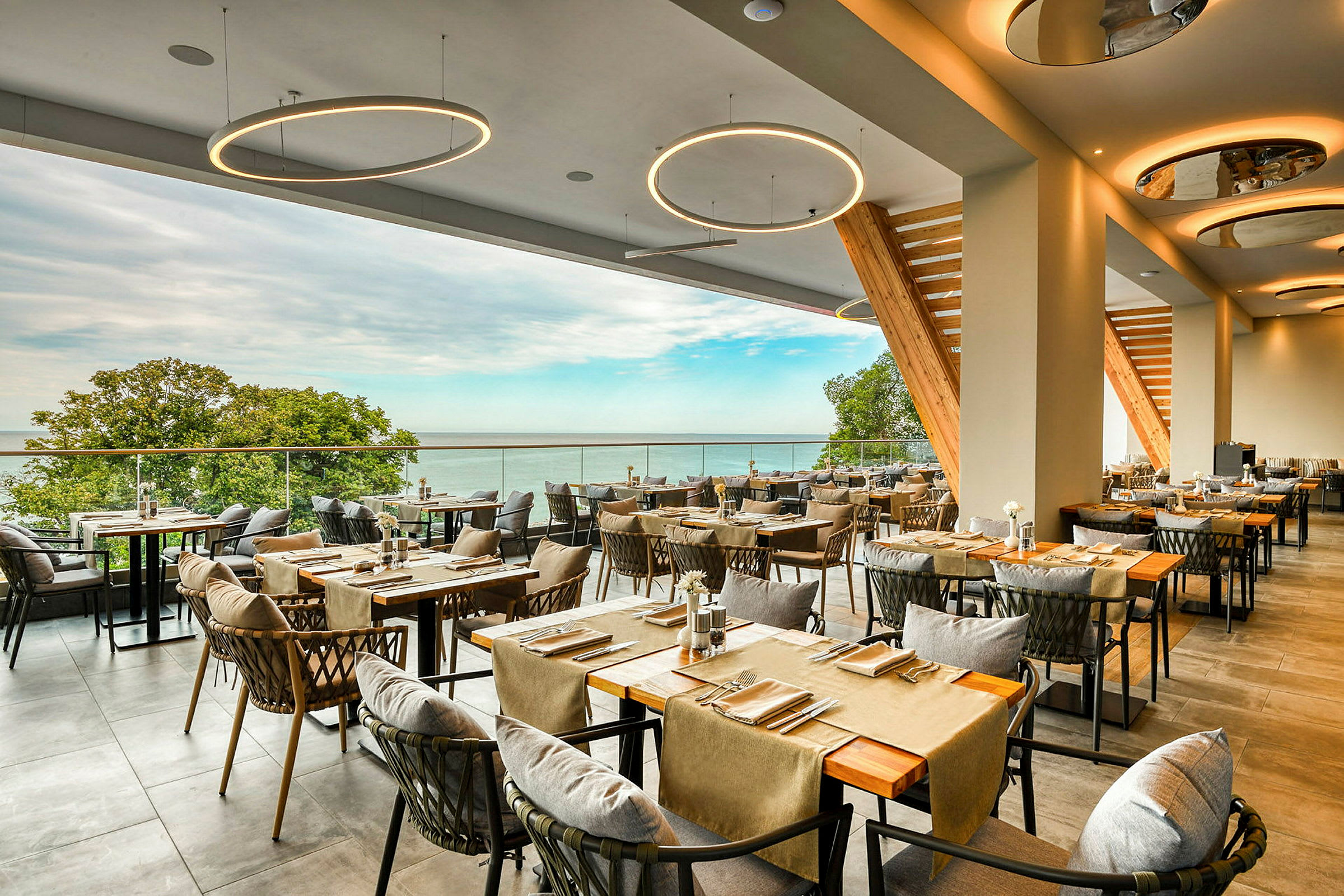 Restaurang med modernt inredda bord och stolar samt utsikt över havet och en grönskande natur. (AI-genererad text)