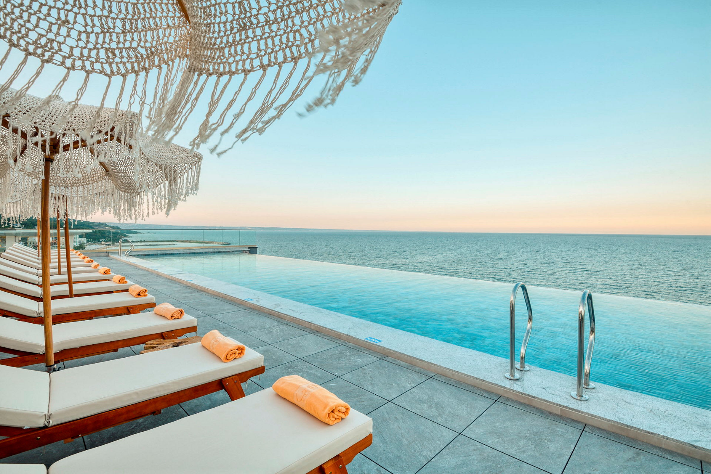 Solstolar med orangea handdukar vid en infinity-pool med utsikt över havet. (AI-genererad text)