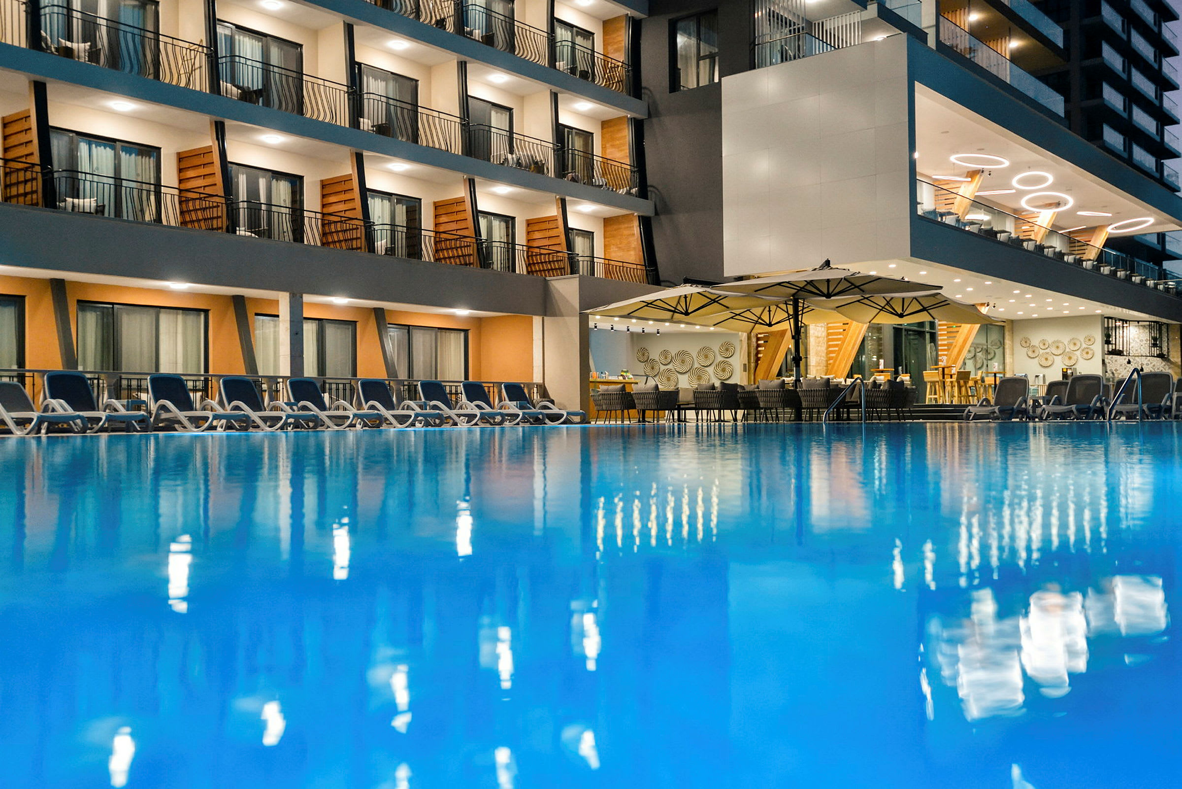 Ett hotell med en utomhuspool, omgivande solstolar och en restaurang med tak och bordsdukning. (AI-genererad text)