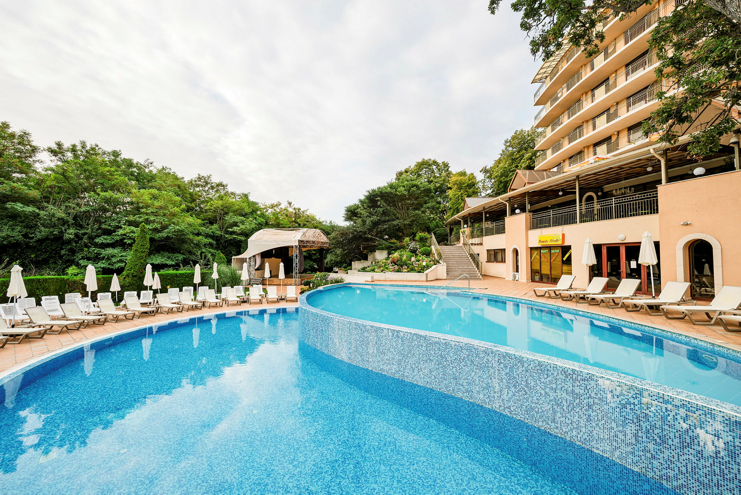 Utomhusområde med en pool, solstolar och ett hotell i bakgrunden. (AI-genererad text)