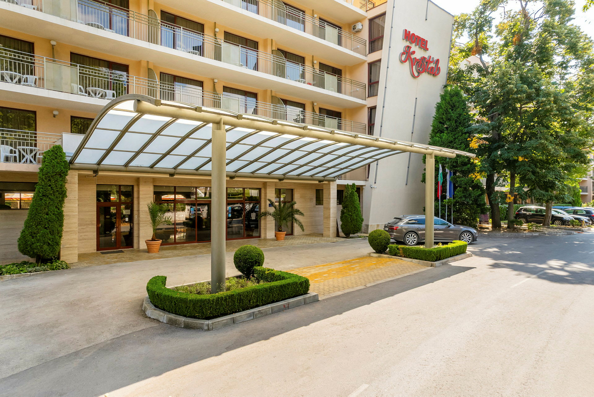 Hotellentré med glasöverhäng och välskött trädgård. (AI-genererad text)