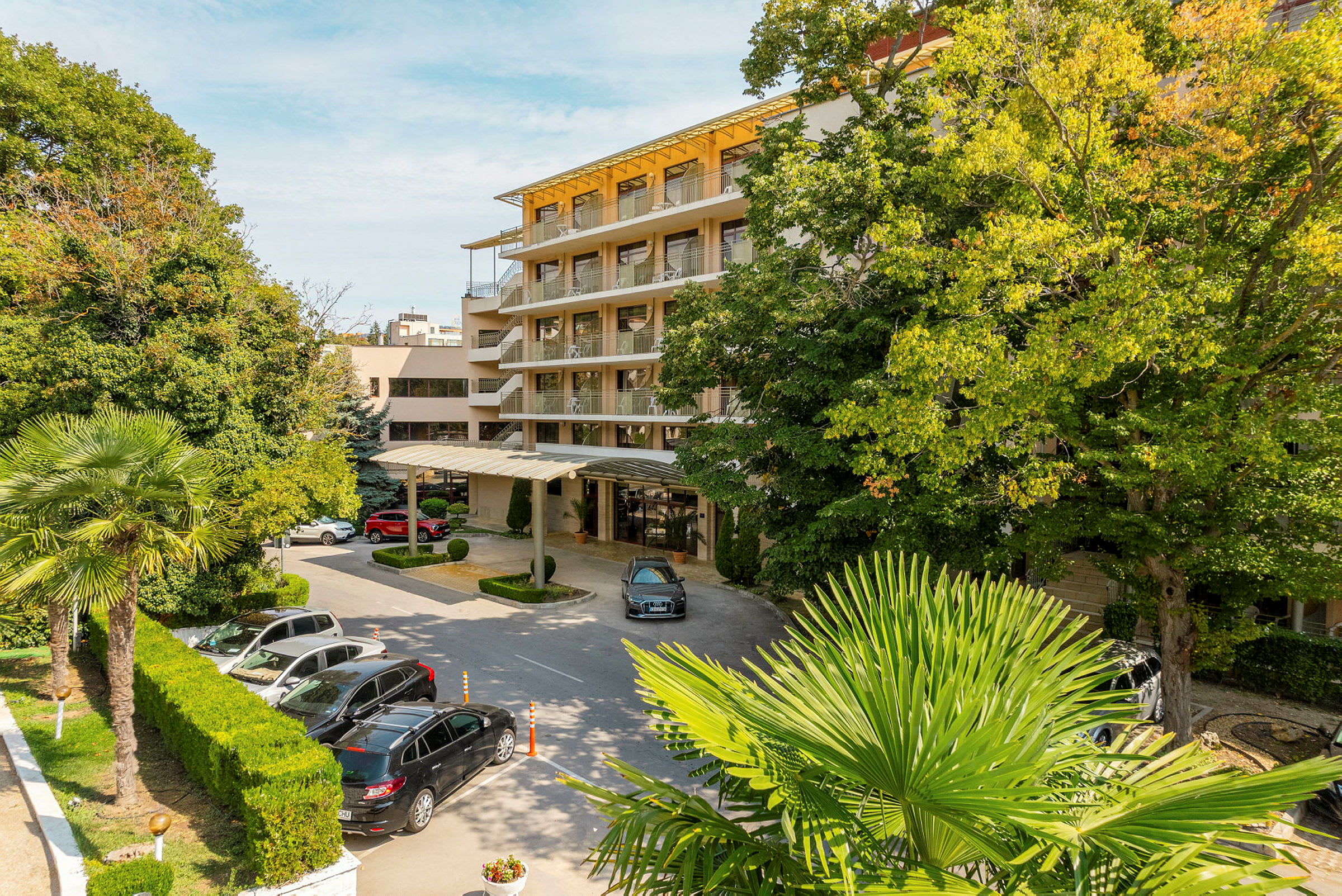 Hotellbyggnad omgiven av träd och bilar parkerade framför. (AI-genererad text)