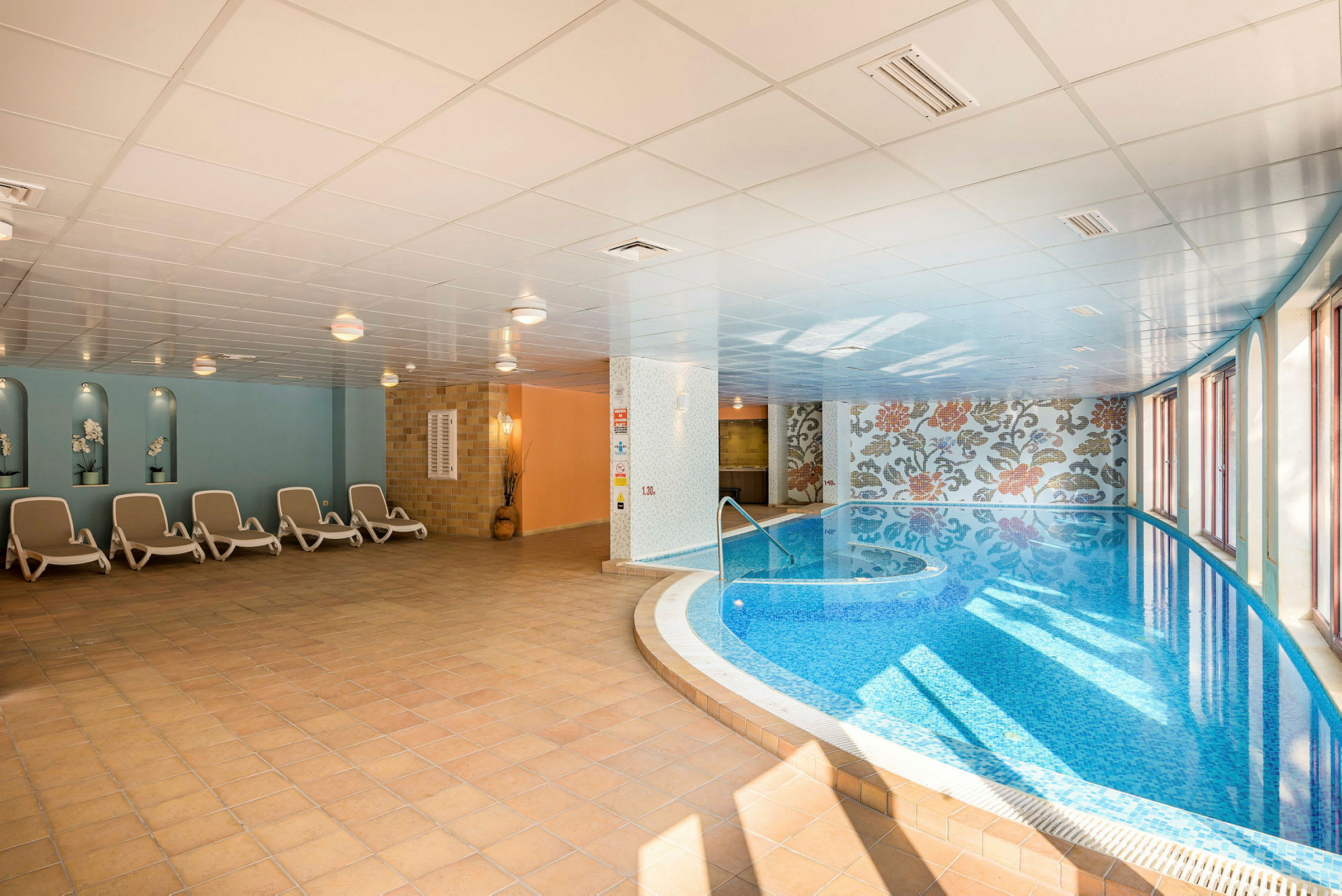 En inomhuspool med blått vatten och solstolar vid sidan. (AI-genererad text)