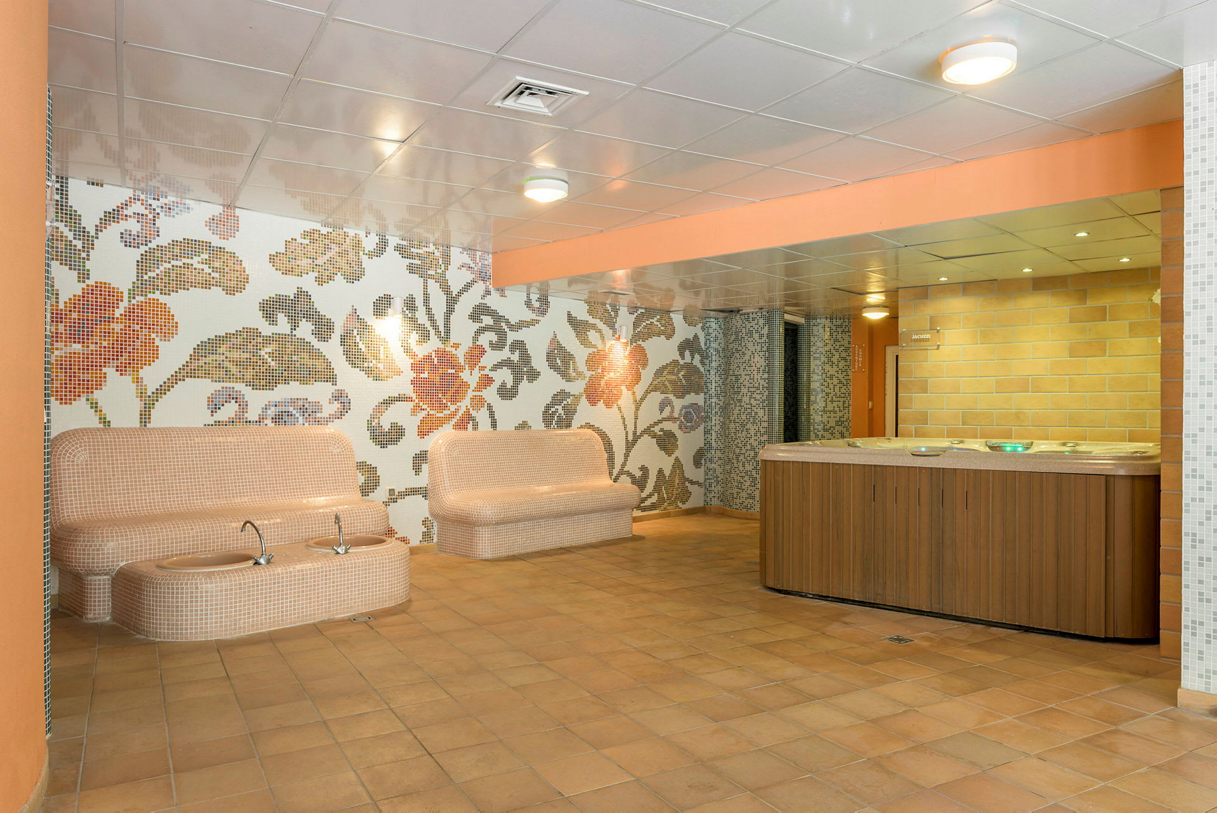 Interiör av ett spaområde med sittplatser, detaljrikt mönster på väggarna och en jacuzzi. (AI-genererad text)