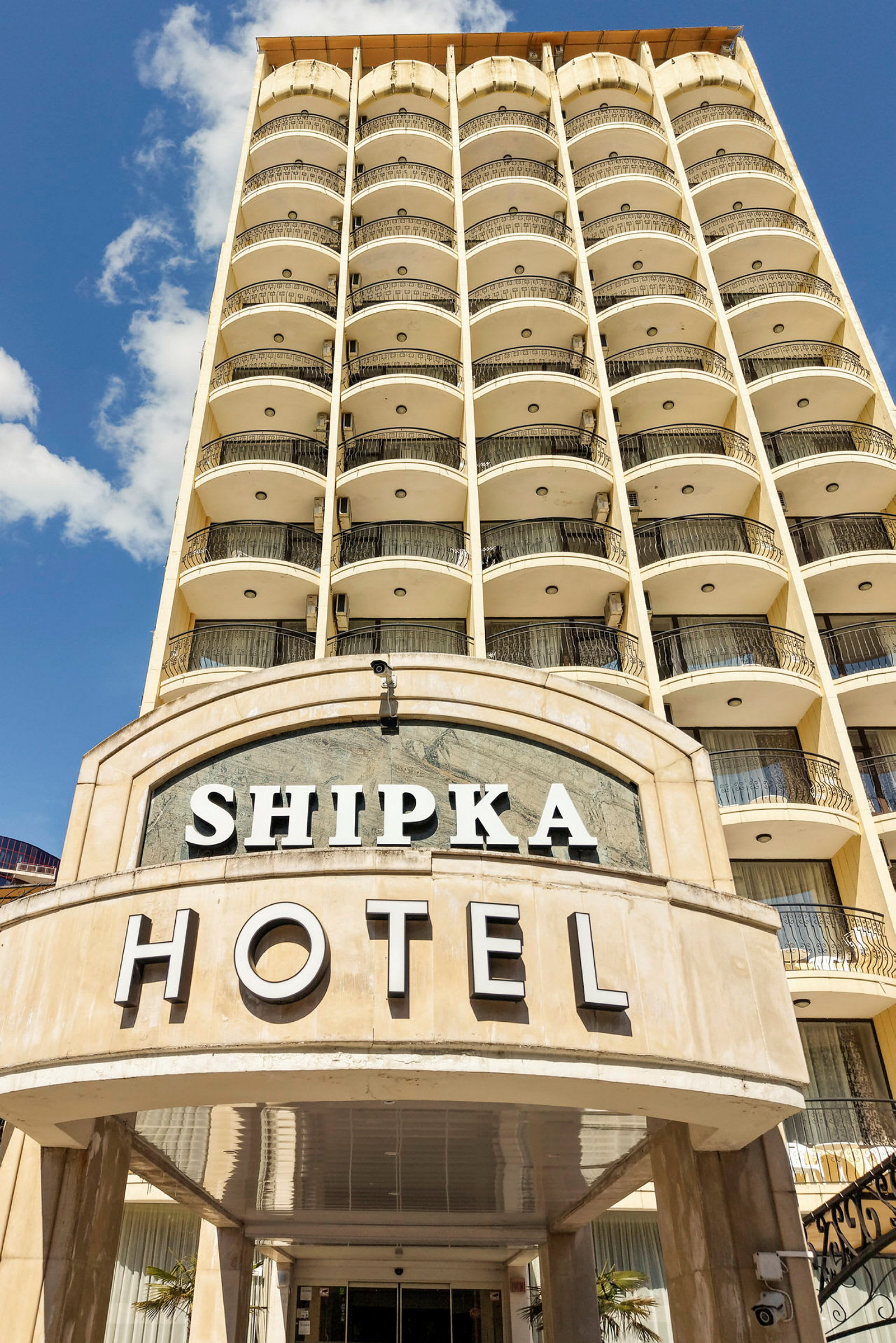 Hotellentré med namnet Shipka, flervåningsbyggnad i bakgrunden. (AI-genererad text)