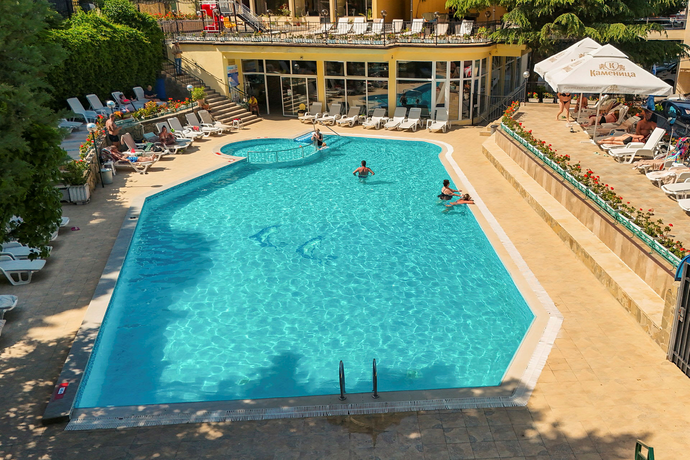 Ett sommarhotellpoolområde med solsängar och människor som badar i poolen. (AI-genererad text)