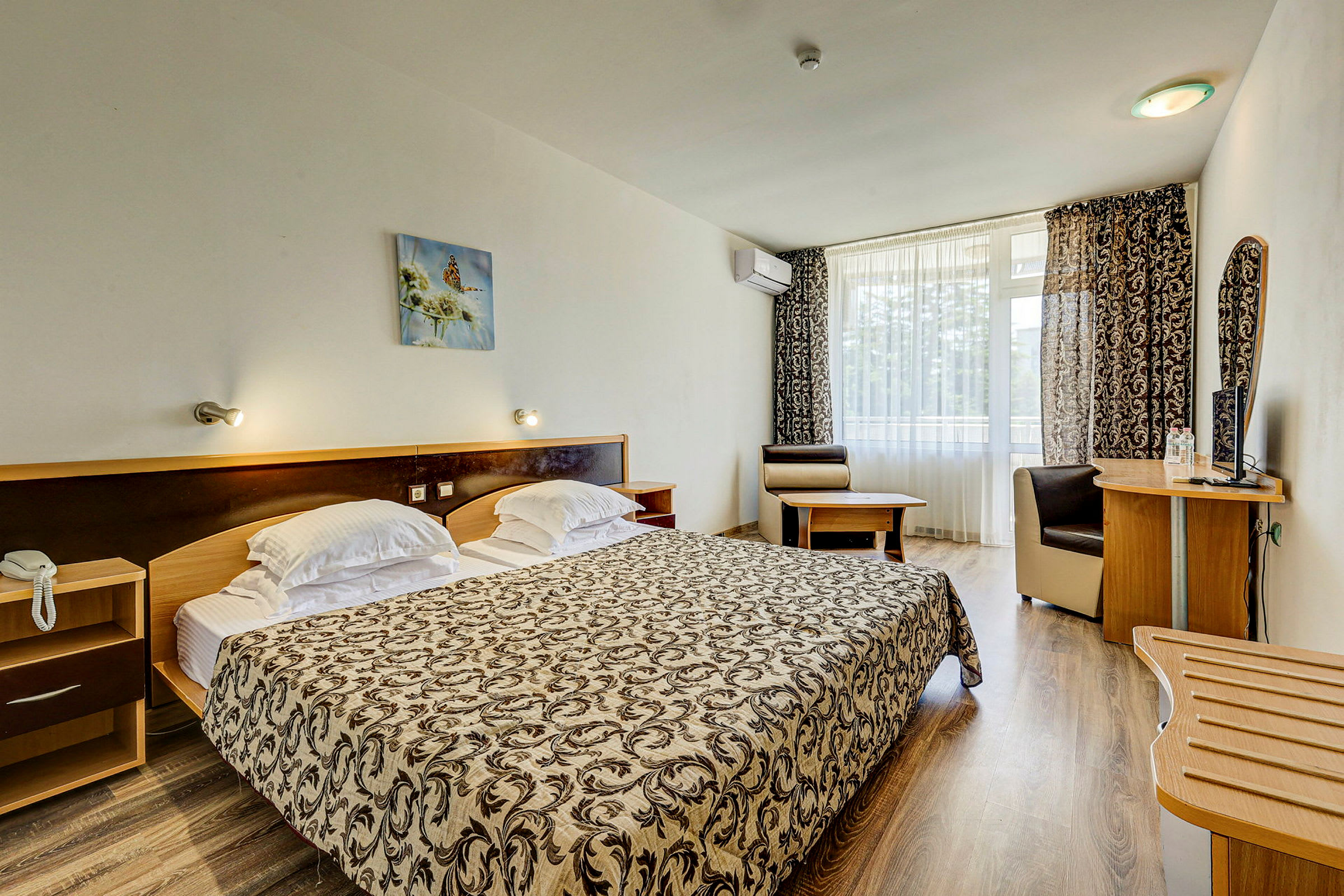 Ett hotellrum med en dubbelsäng, skrivbord, stol och ett stort fönster med gardiner. (AI-genererad text)
