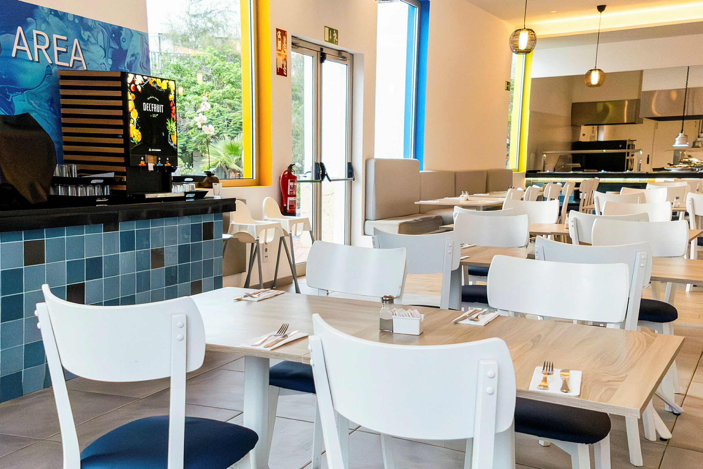 En modern restaurang med vita bord och stolar. En juiceautomat syns till vänster. (AI-genererad text)