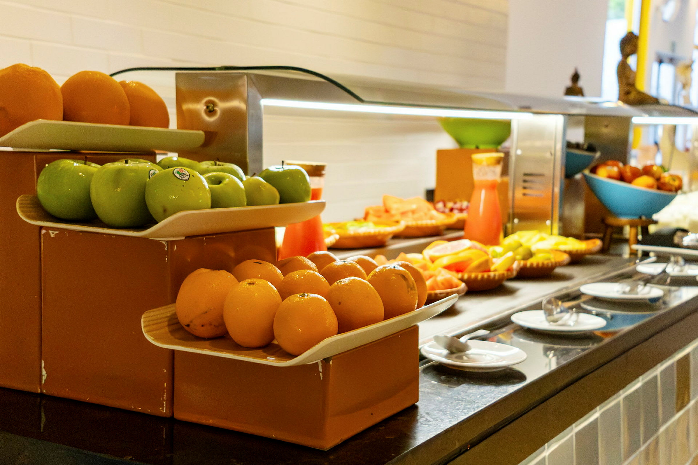 Fruktbuffé med gröna äpplen, apelsiner och annan frukt samt juicekanna. (AI-genererad text)