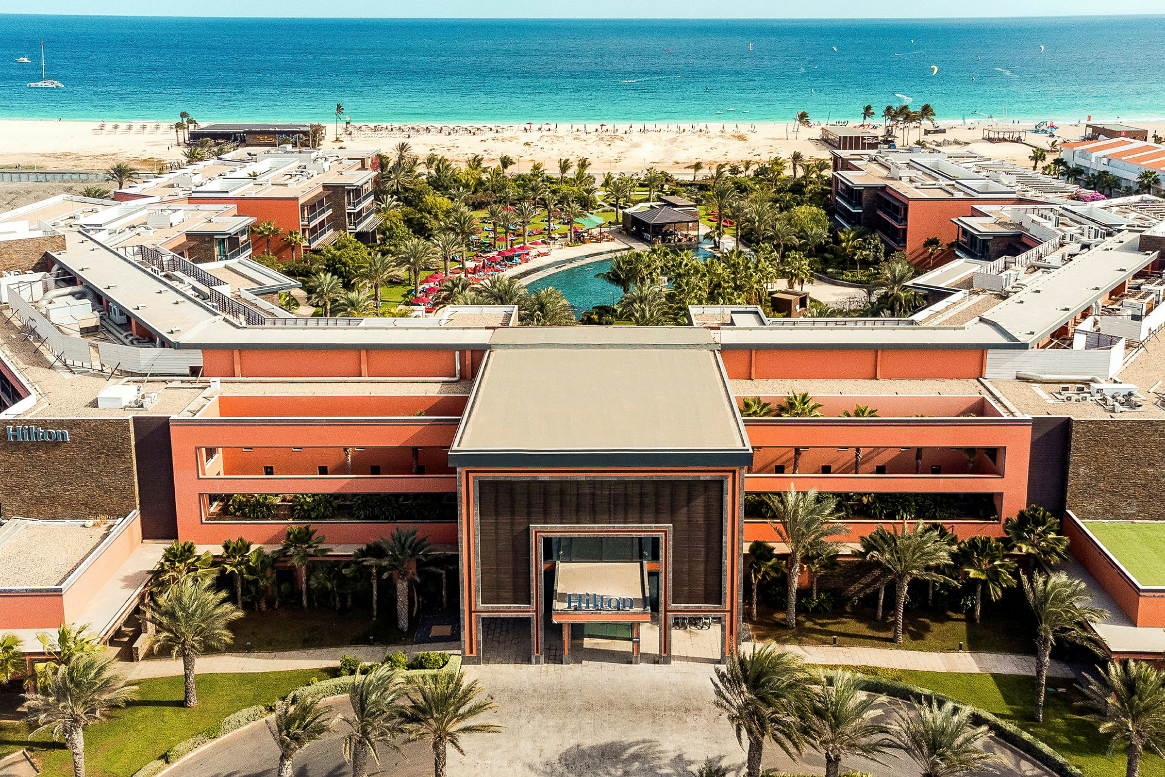 Flygfoto av hotellbyggnad med poolområde och strandutsikt. (AI-genererad text)