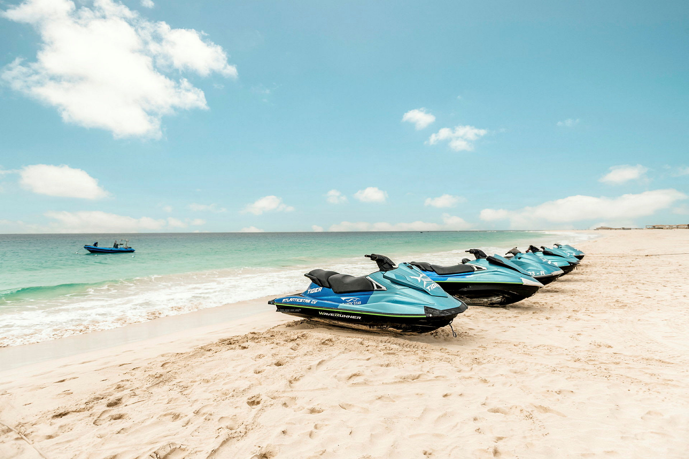 Flera blå jet-skidor står uppradade på en sandstrand intill havet. (AI-genererad text)
