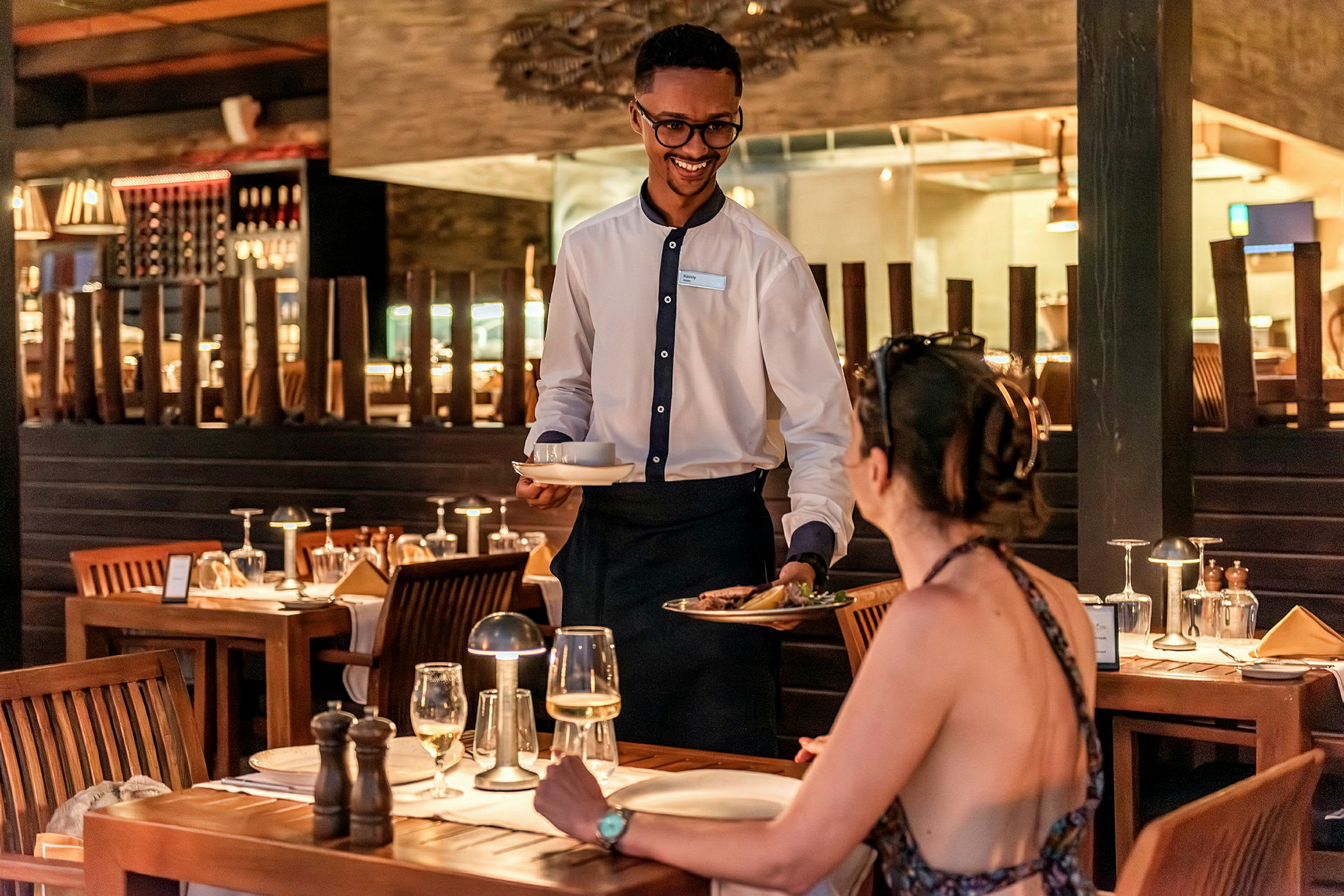Servitör serverar mat till en kvinna vid ett restaurangbord. (AI-genererad text)