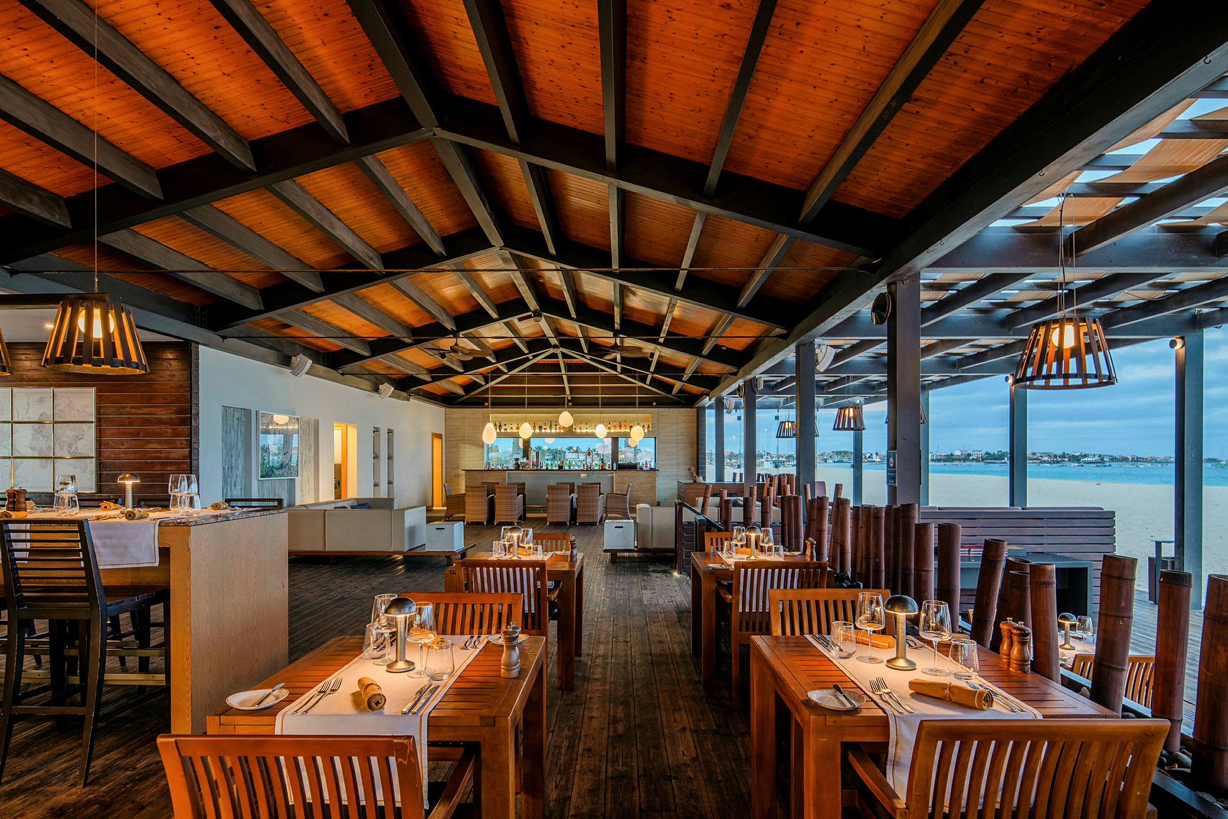 En restaurang med träinredning och dukade bord med tallrikar och glas, med en öppen vy mot utomhusmiljön. (AI-genererad text)
