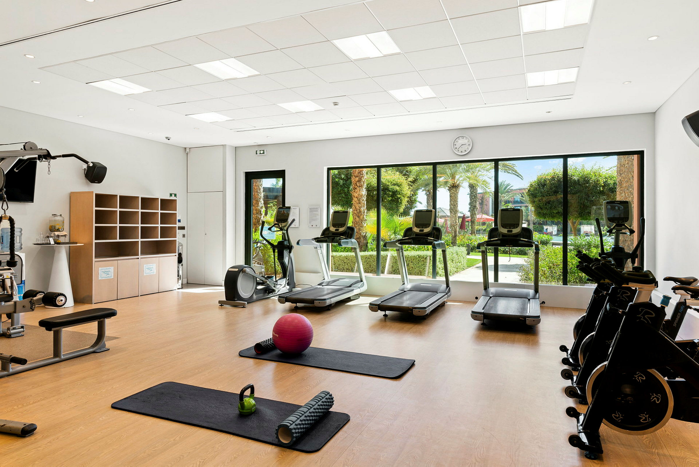Ett ljust gym med träningsmaskiner och fönster med utsikt mot en trädgård. (AI-genererad text)