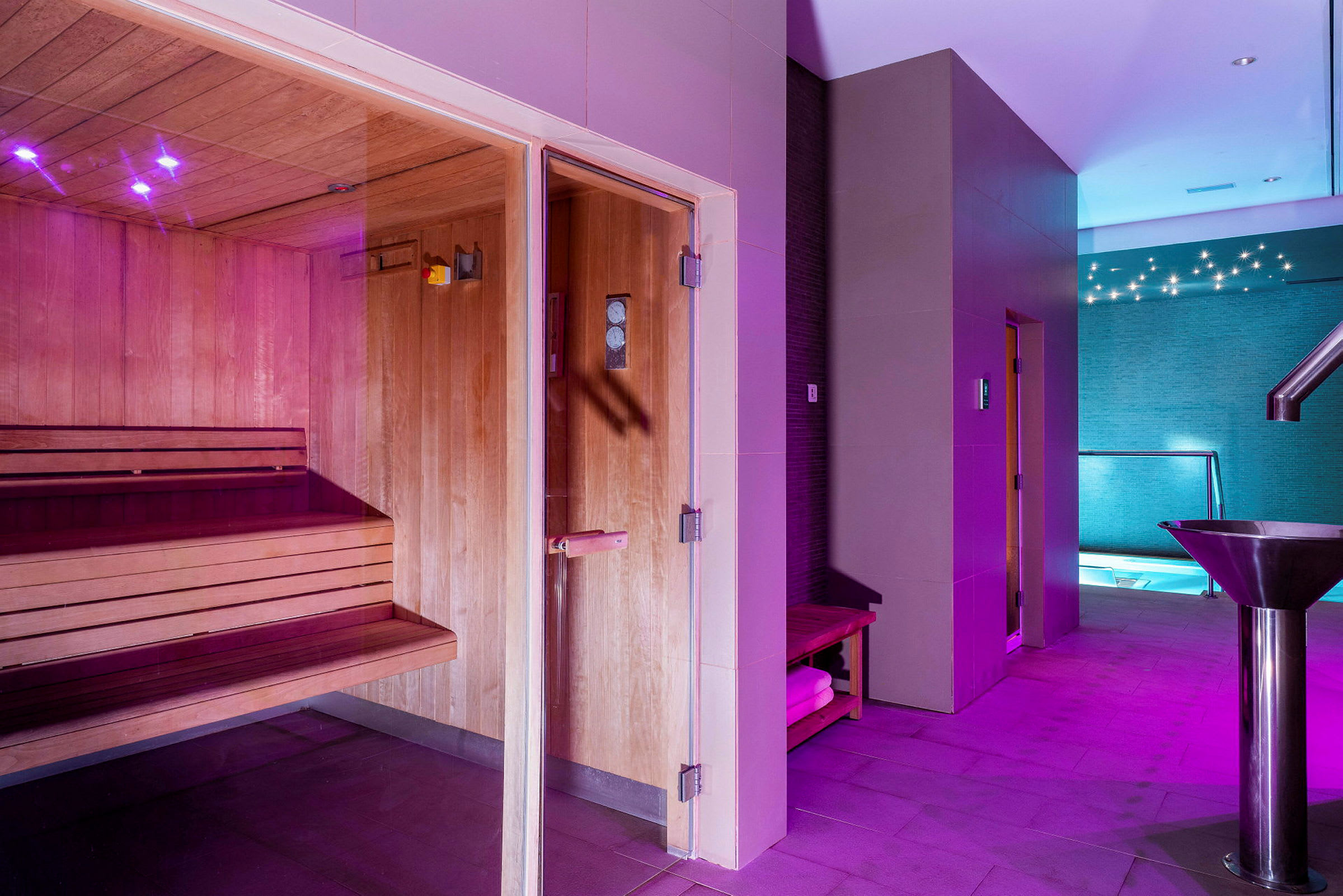 Ett spa som visar en bastu med träpaneler, en gång med belysning och utsikt till en pool. (AI-genererad text)