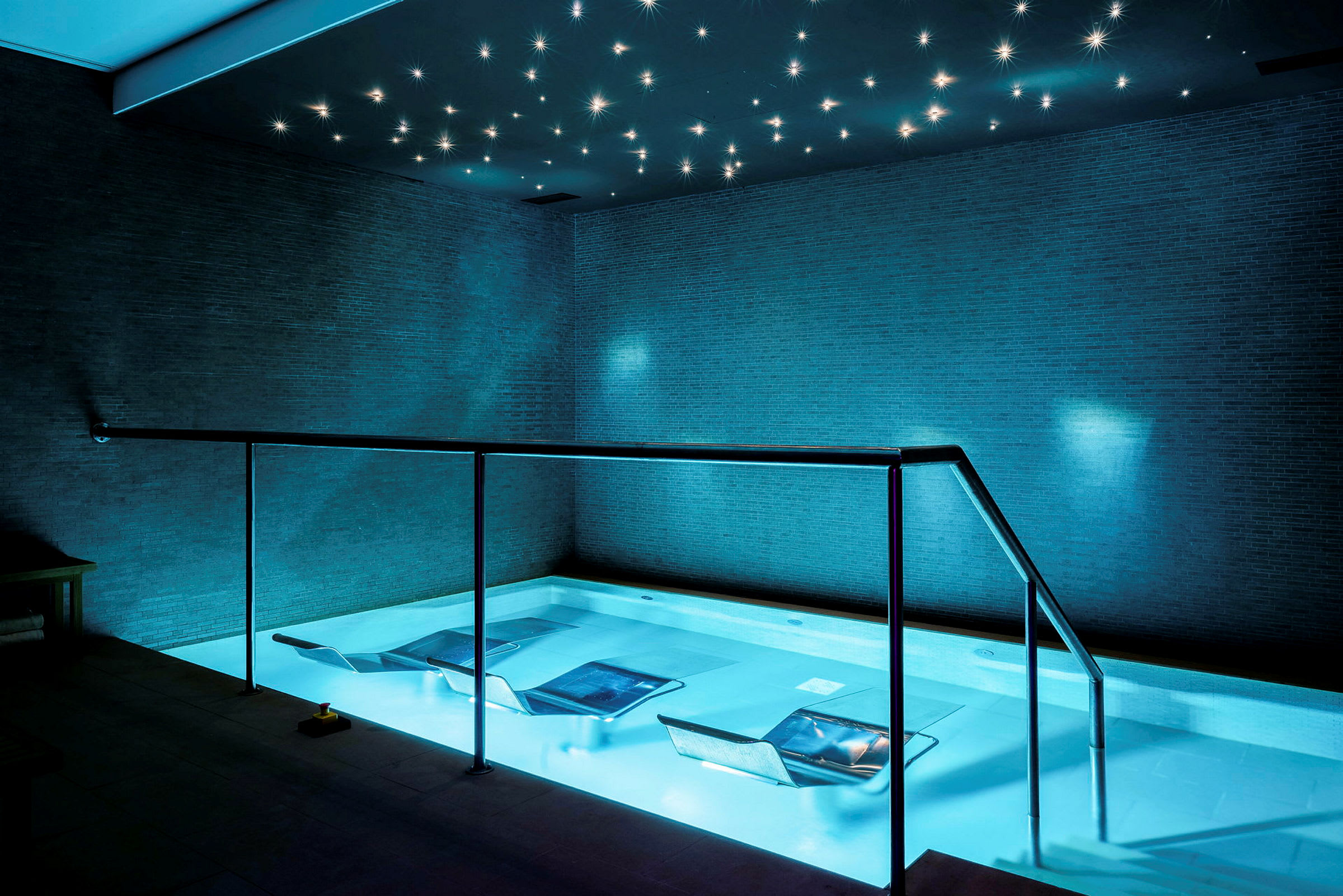 En pool i ett spa med avslappningsstolar i vattnet och en stjärnformad ljusinstallation i taket. (AI-genererad text)