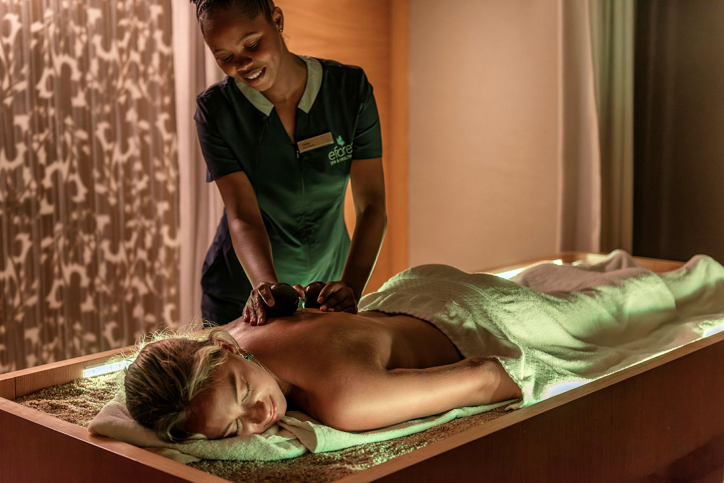 En person får en massagebehandling av en massageterapeut som använder varma stenar i ett avslappnande rum. (AI-genererad text)