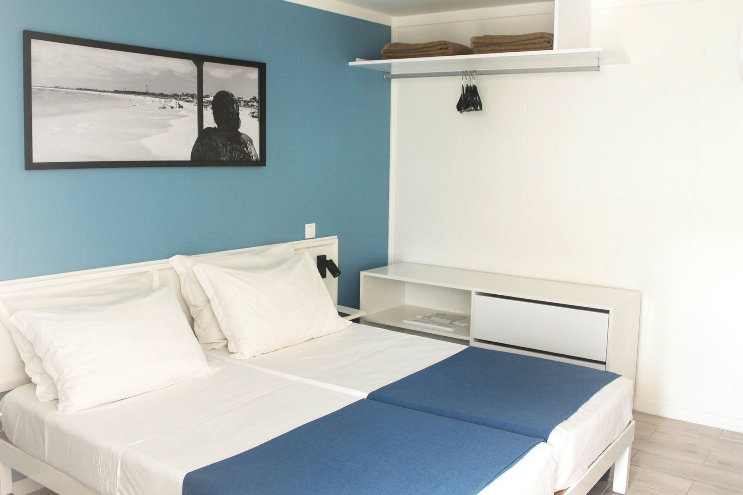 Hotellrum med två enkelsängar, vita väggar och en blå fondvägg. (AI-genererad text)
