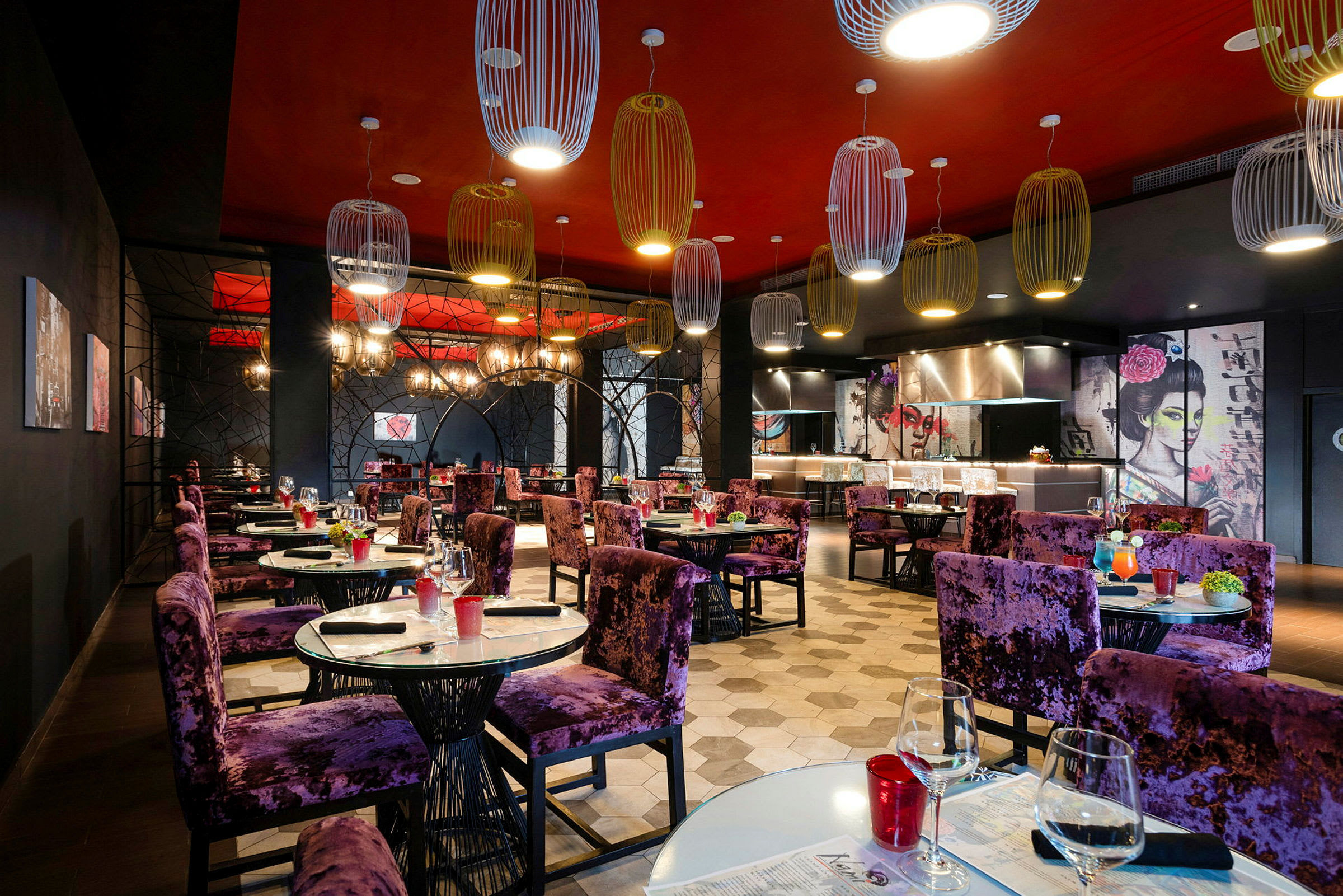 En restaurang med elegant inredning och lila stolar vid dukade bord. Väggarna har konstnärliga motiv och taket är dekorerat med moderna lampor. (AI-genererad text)