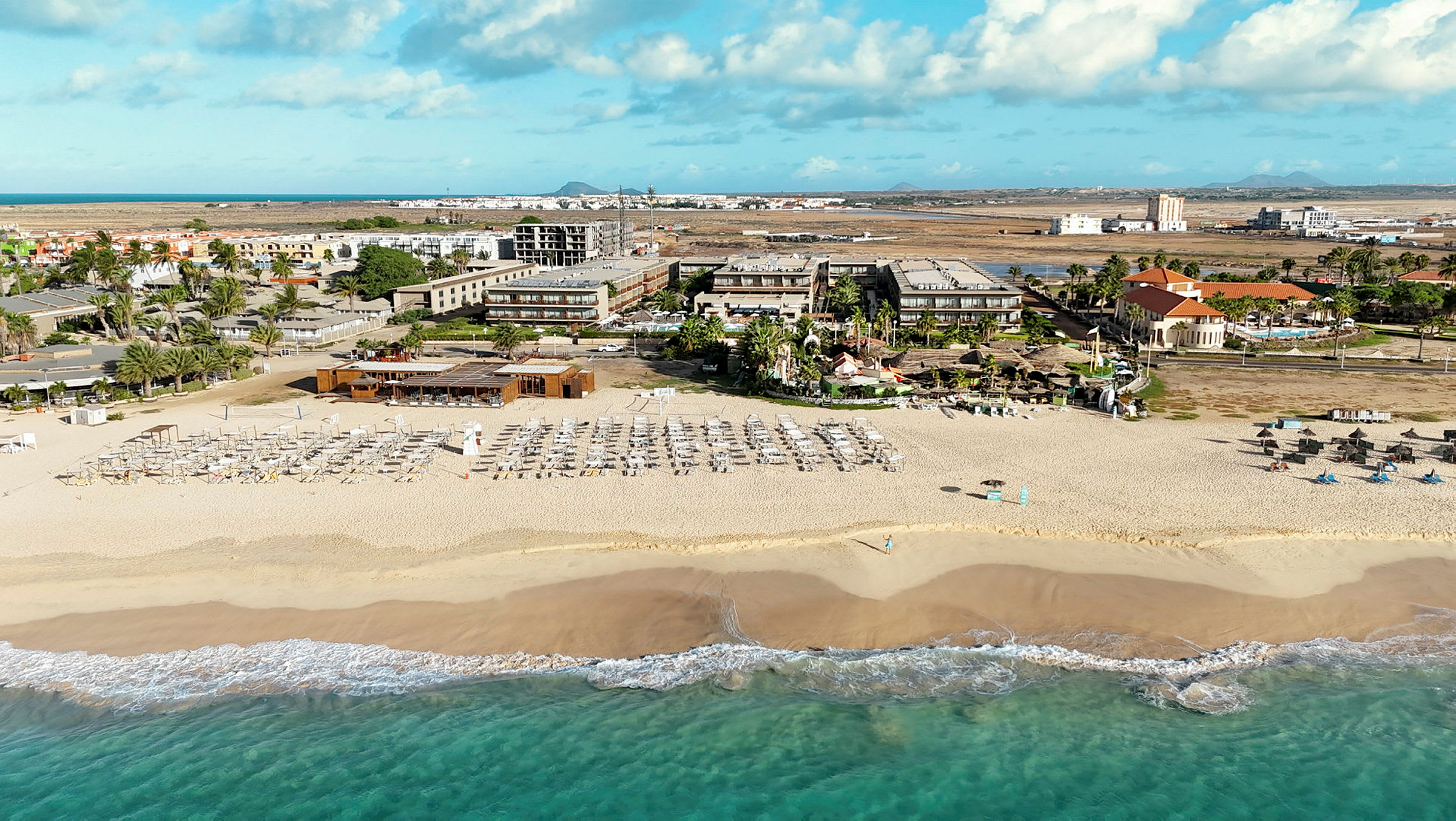 Bild av en sandstrand med solstolar och parasoller, hotellbyggnader i bakgrunden. (AI-genererad text)