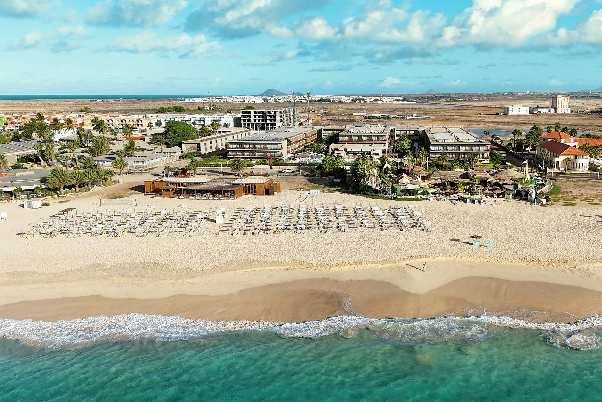 Strand med solstolar och parasoller framför hotell och byggnader. (AI-genererad text)