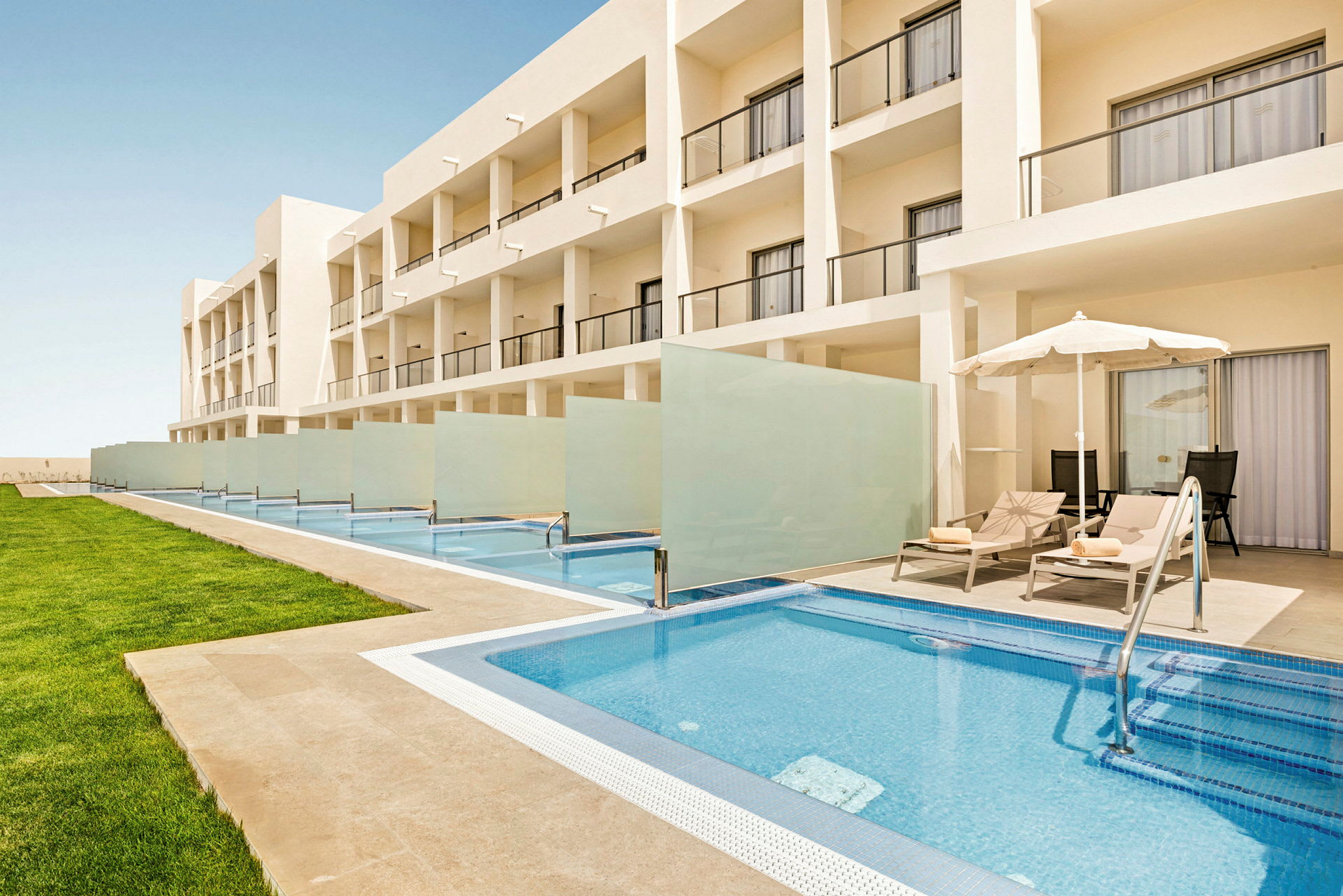 Bild som visar en modern hotellbyggnad med privata pooler framför varje rum och solstolar under parasoller bredvid poolerna. (AI-genererad text)