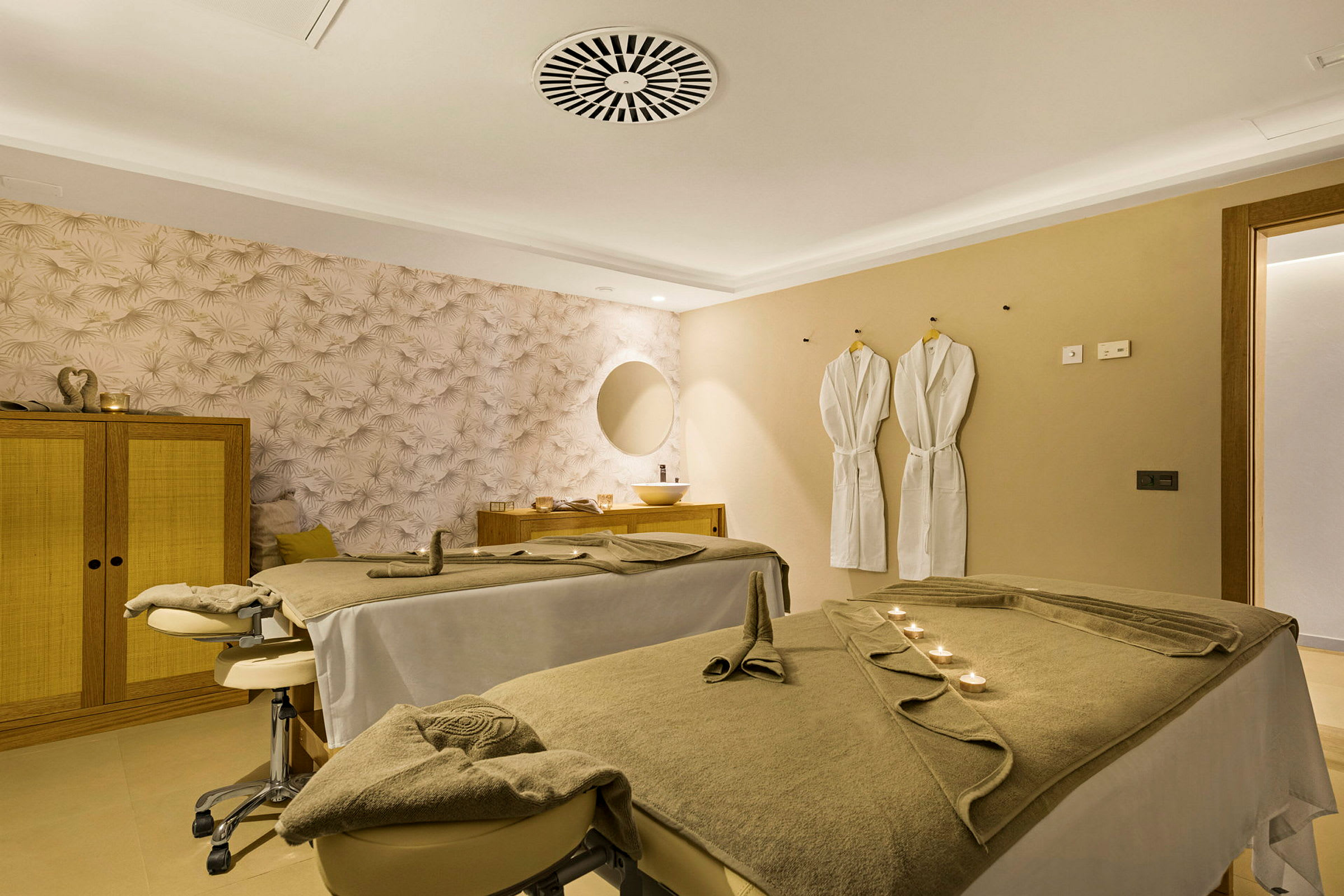 Ett spa-rum med två massagebänkar, två badrockar på väggen och en dekorativ vägg. (AI-genererad text)