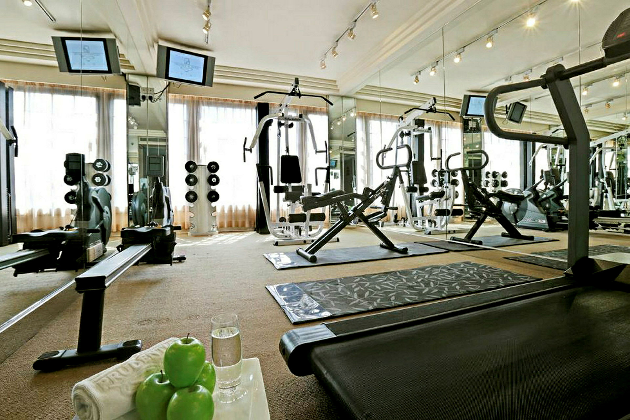 Ett gym med träningsmaskiner, vikter och speglar. På ett bord ligger gröna äpplen och ett glas vatten. (AI-genererad text)