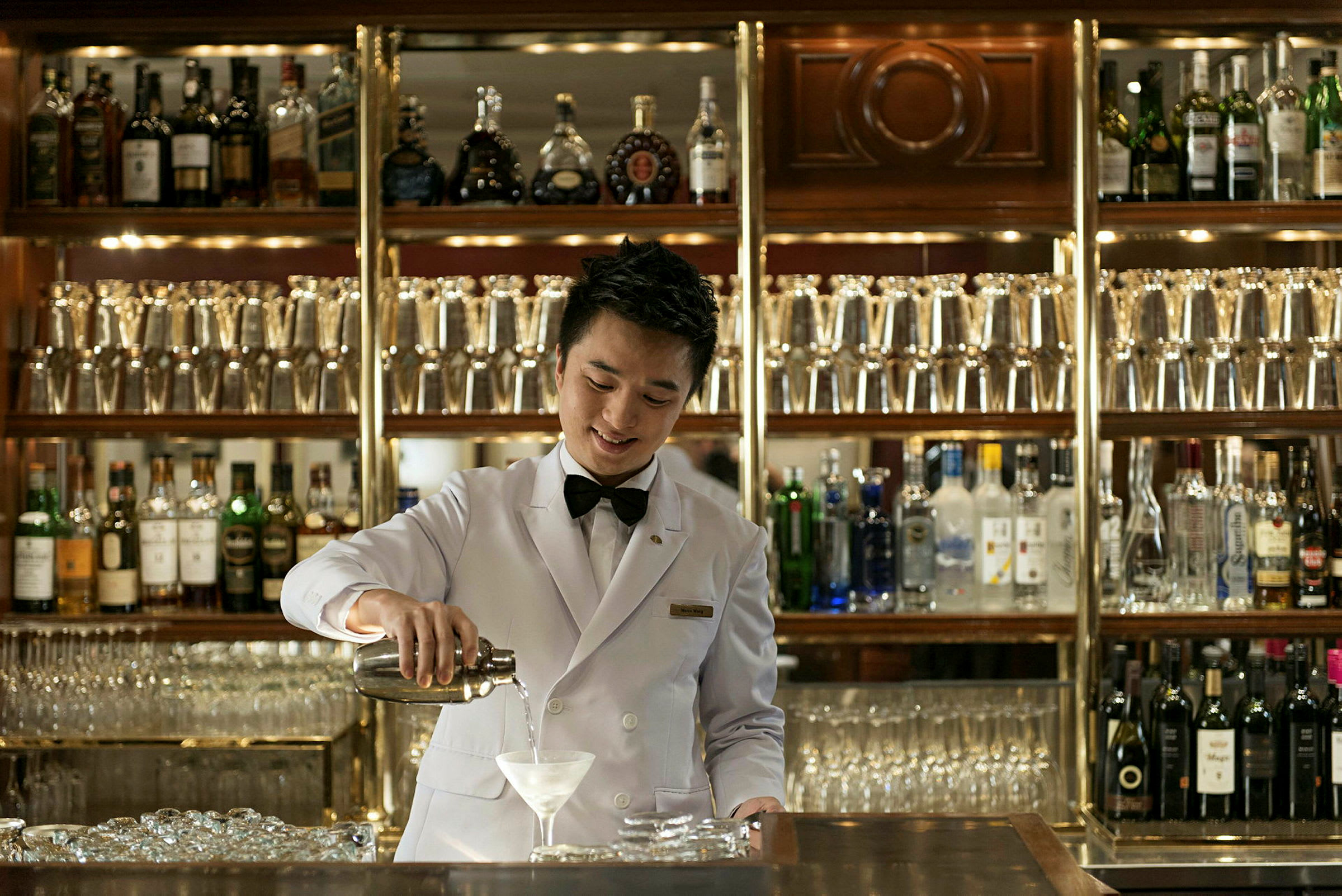 En bartender klädd i vit kavaj som serverar en drink framför en välfylld bar. (AI-genererad text)