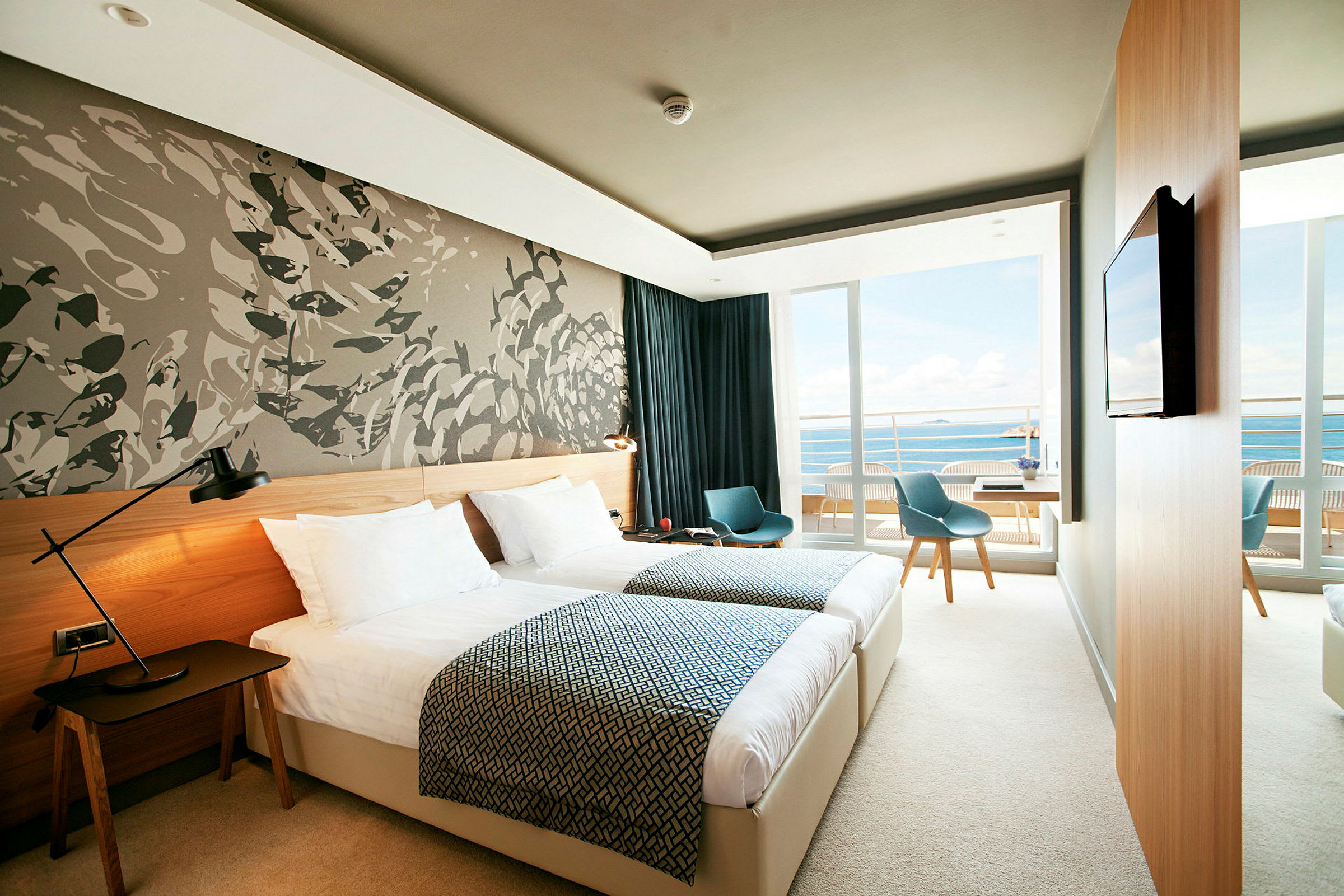 Ett modernt hotellrum med två enkelsängar, en väggdekoration, och en balkong med utsikt över havet. (AI-genererad text)