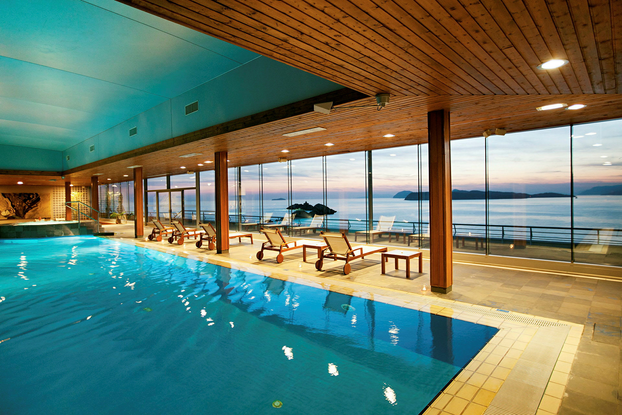 En inomhuspool i ett spa med utsikt mot havet genom stora panoramafönster. (AI-genererad text)