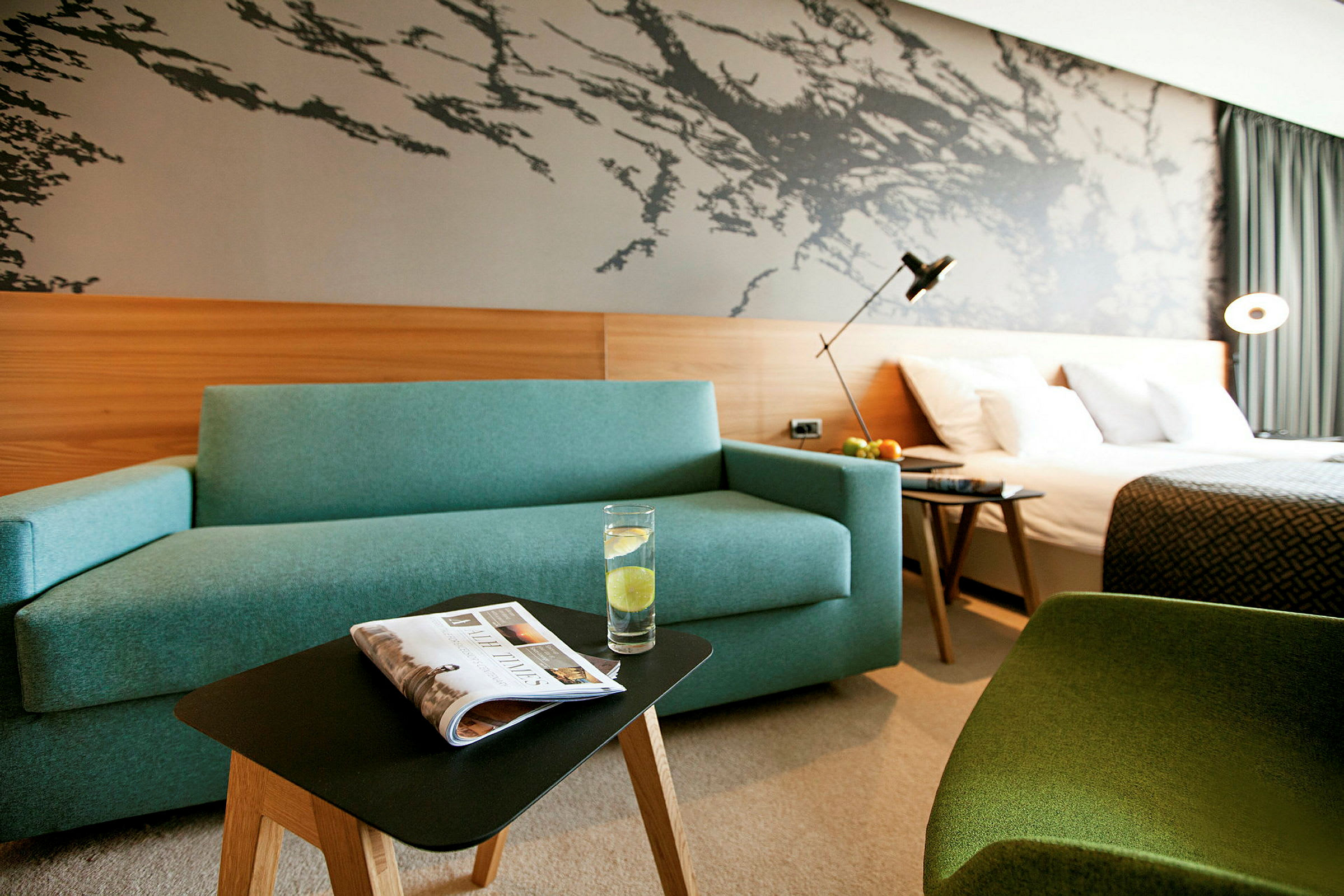 Hotellrum med en blå soffa, ett litet bord med ett glas vatten, en säng och en dekorativ vägg. (AI-genererad text)
