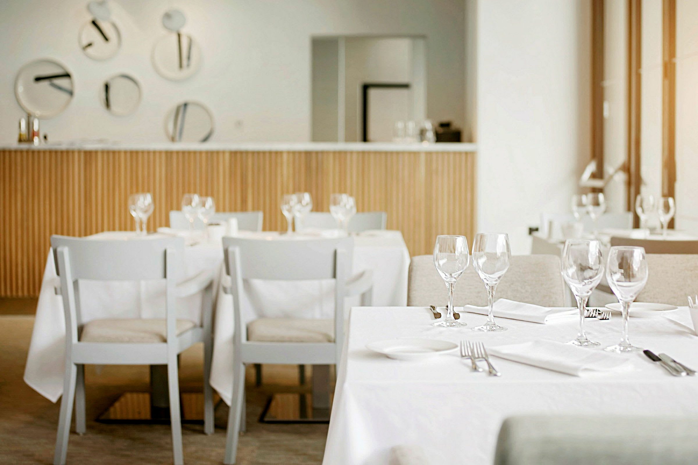 Ett modernt och ljust restauranginteriör med dukade bord och vita stolar. På bordet finns glas, bestick och servetter. (AI-genererad text)