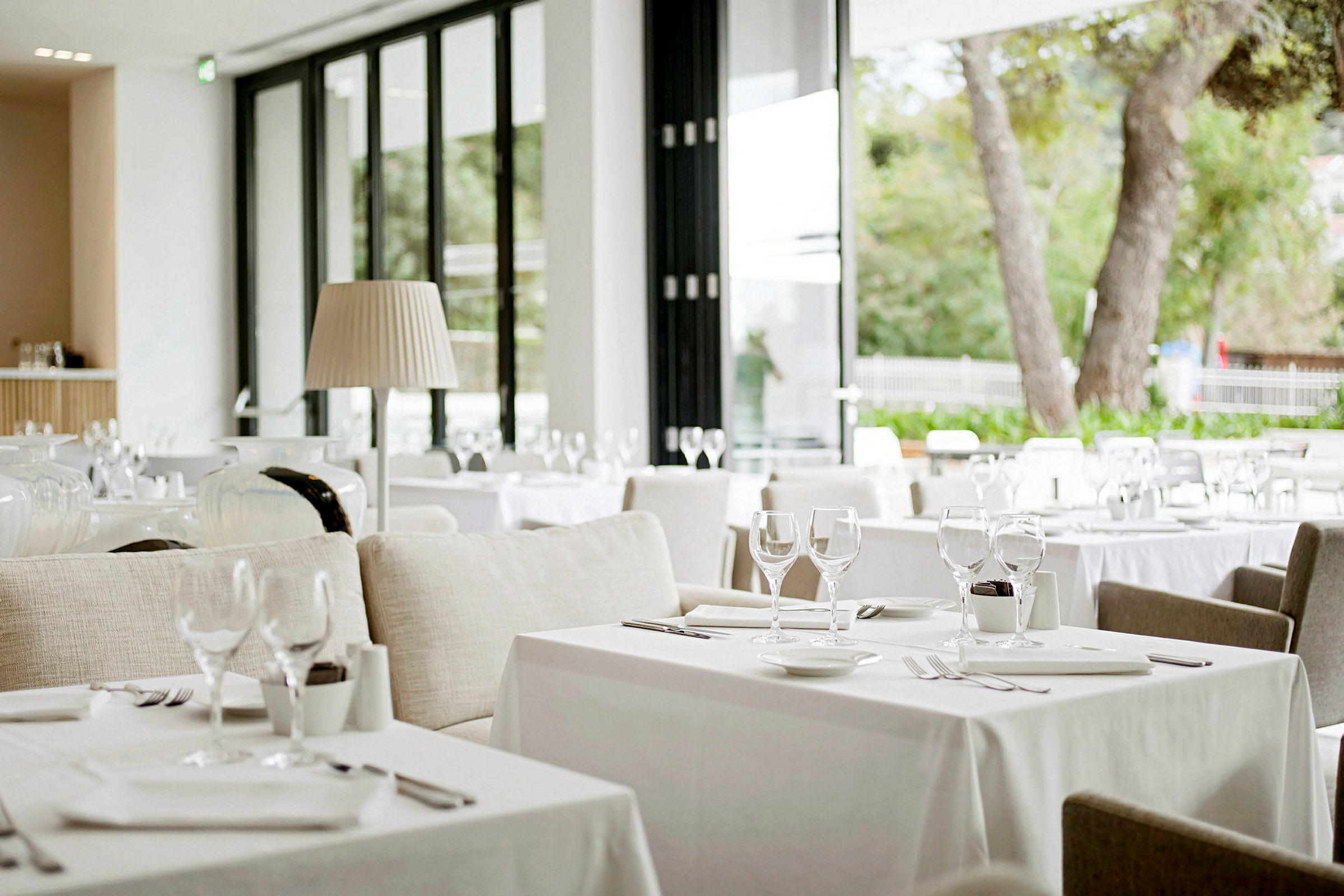 Bild på en modern och ljus restaurang med dukade bord och stora glasfönster som släpper in naturligt ljus. (AI-genererad text)
