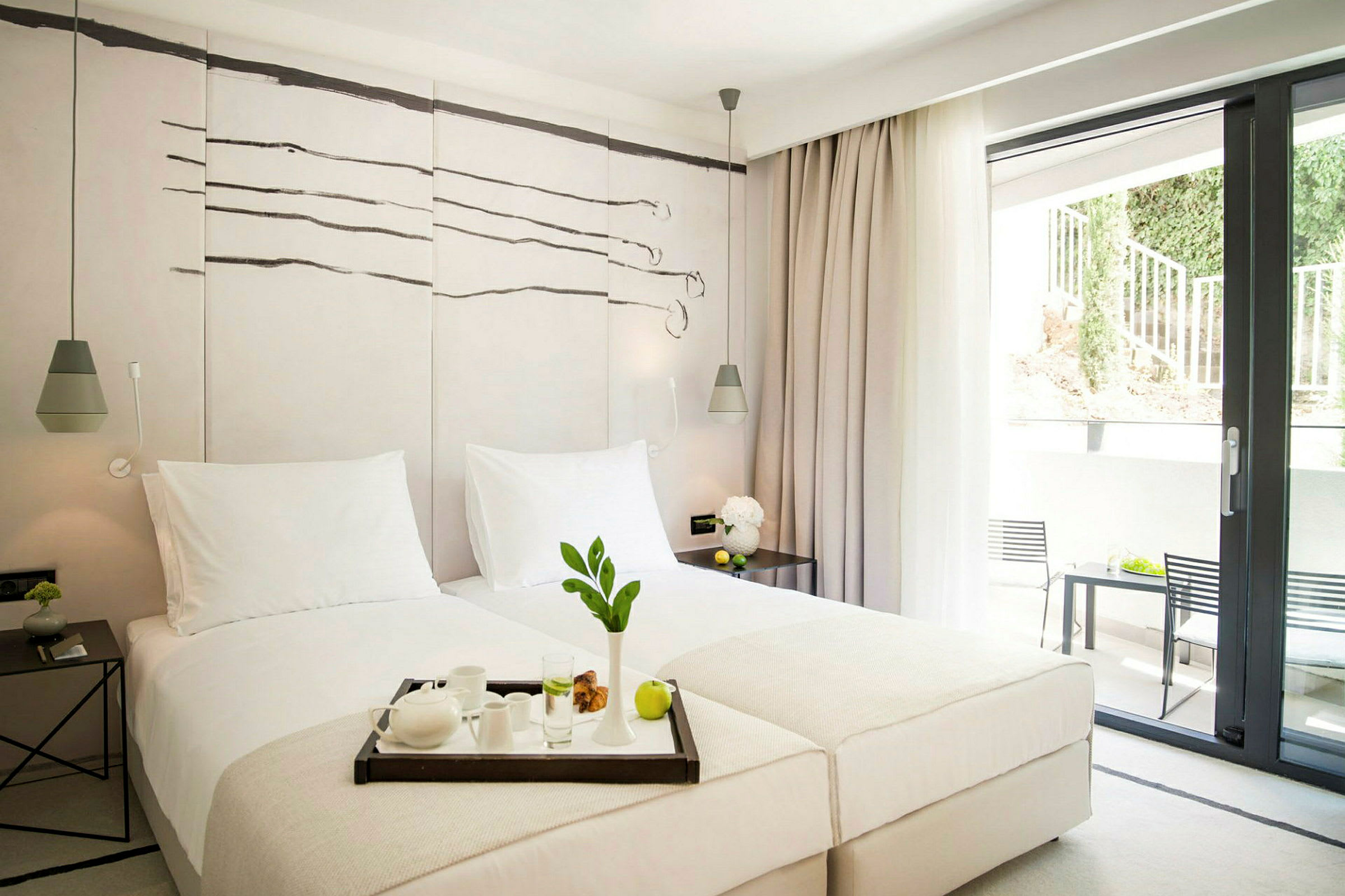 Ett ljust och modernt hotellrum med två enkelsängar, stilren inredning och en stor glasdörr som leder till en balkong. (AI-genererad text)