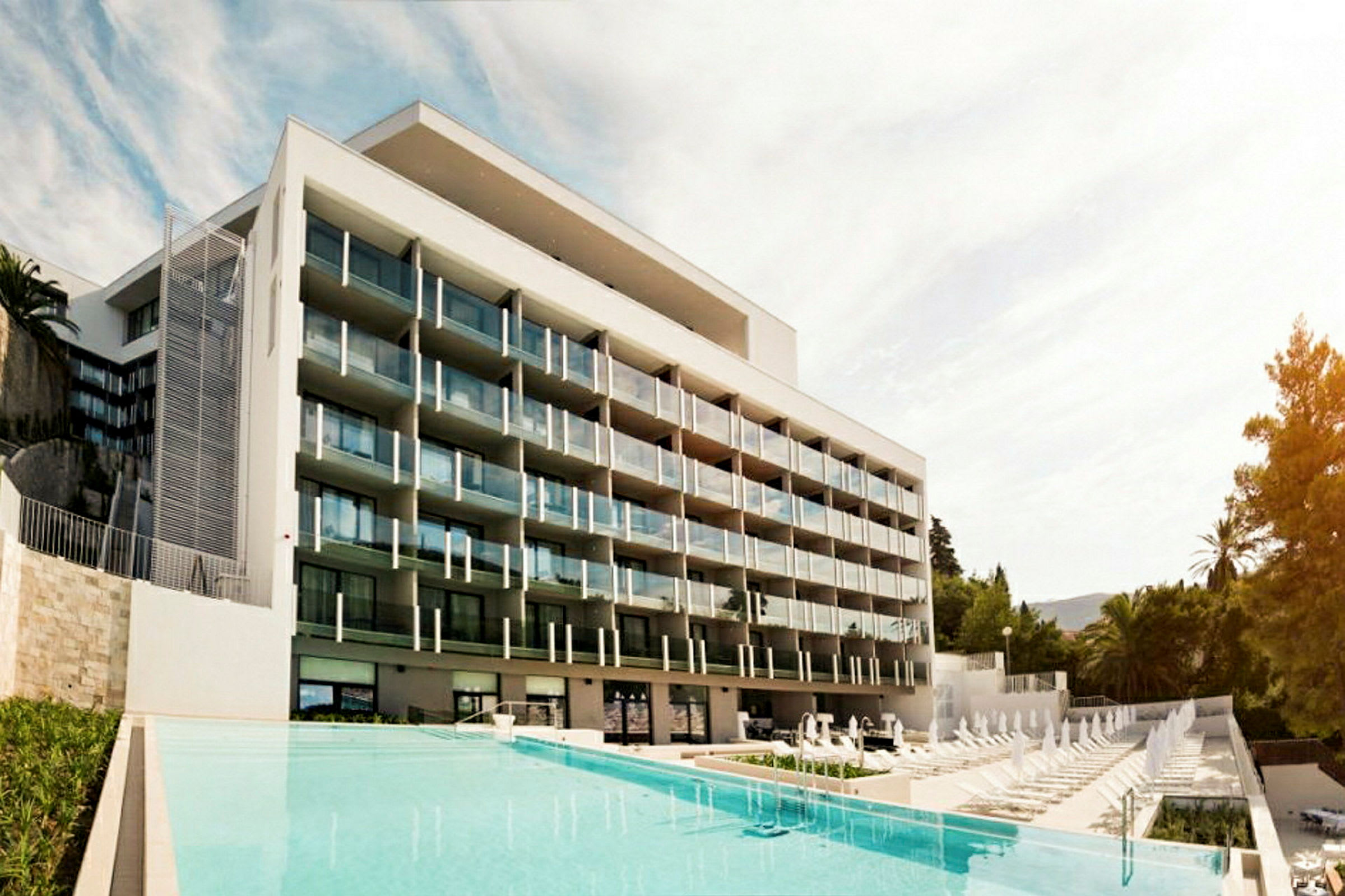 Ett modernt hotell med flera balkonger framför en pool. (AI-genererad text)