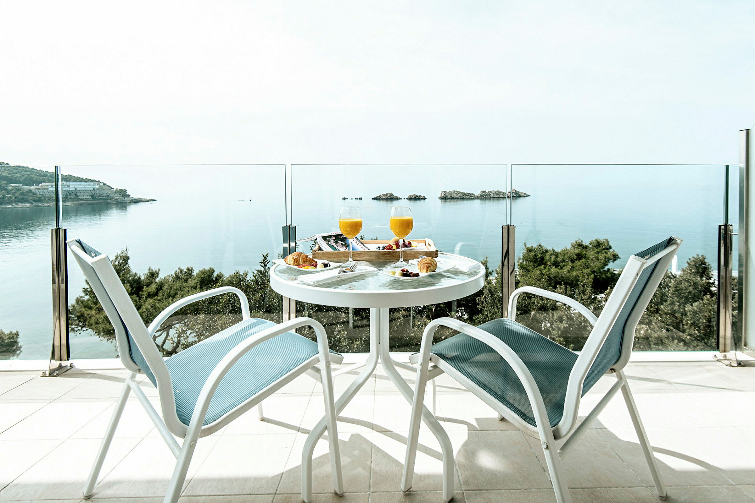 Två stolar och ett bord med frukost är placerade på en terrass med utsikt över havet och några små öar. (AI-genererad text)